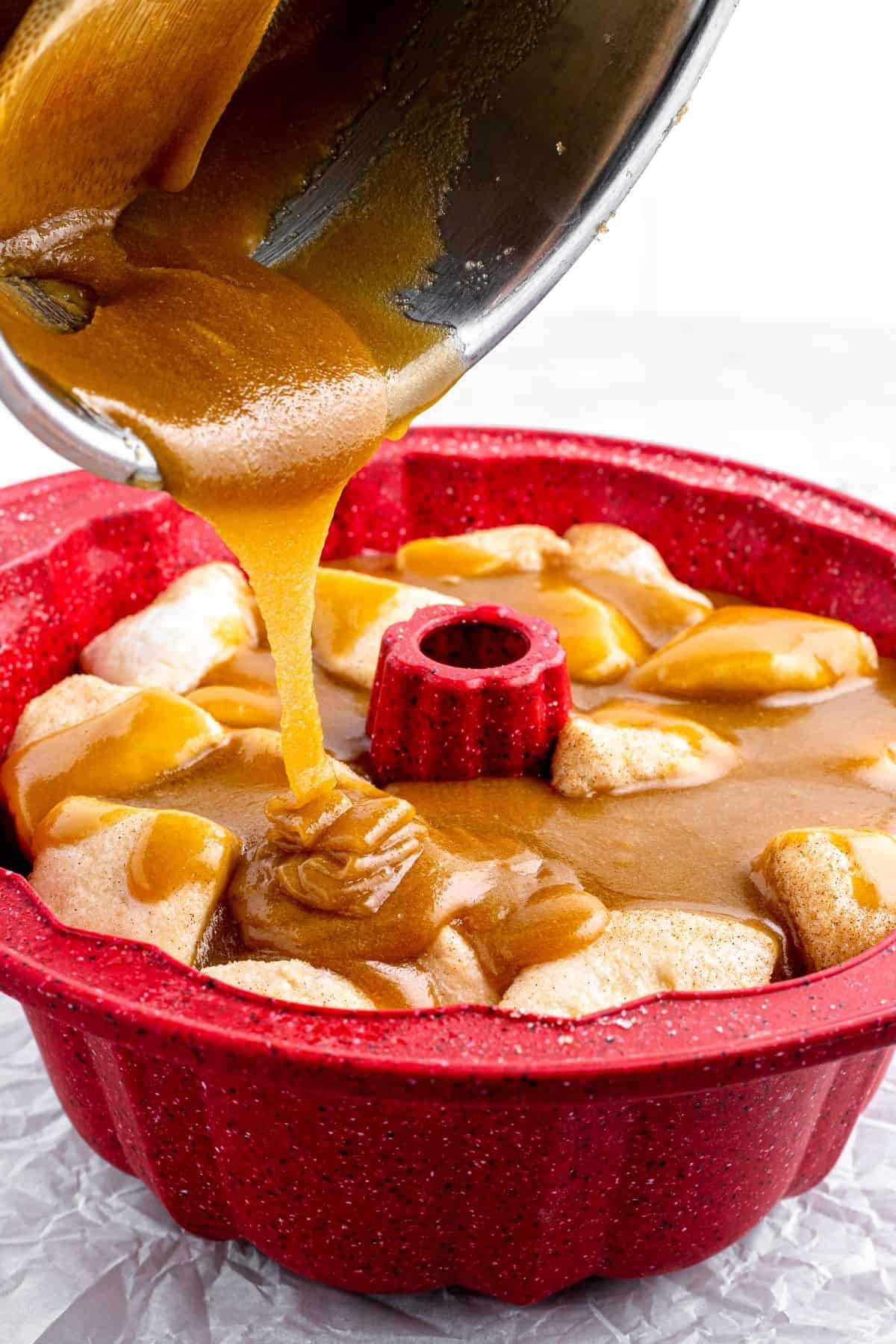 A thick brown-sugar-butter mixture is poured from a saucepan over biscuit dough pieces in a Bundt pan.