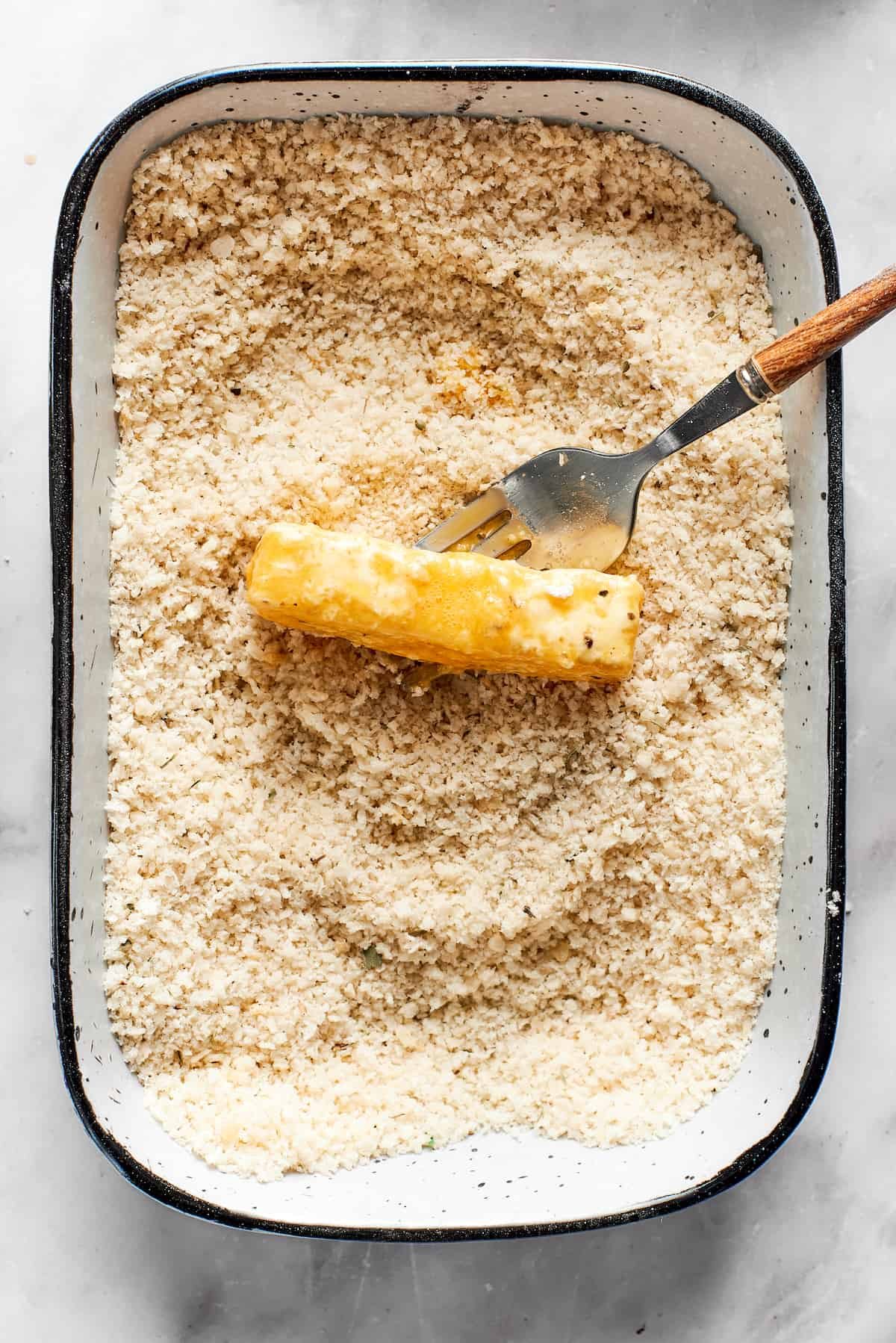 A tray of breadcrumbs with a piece of mozzarella in it.