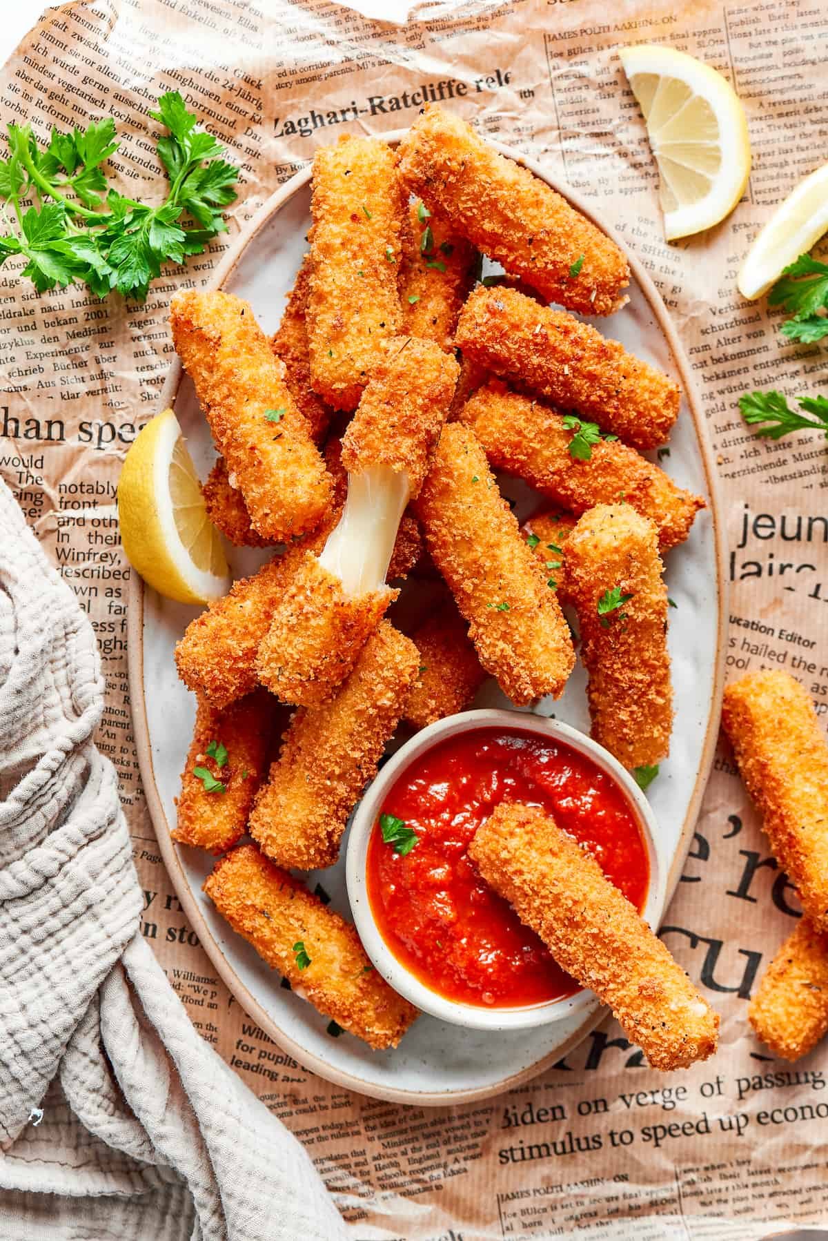 A platter of mozzarella sticks with one cut in half and one dipped in tomato sauce.