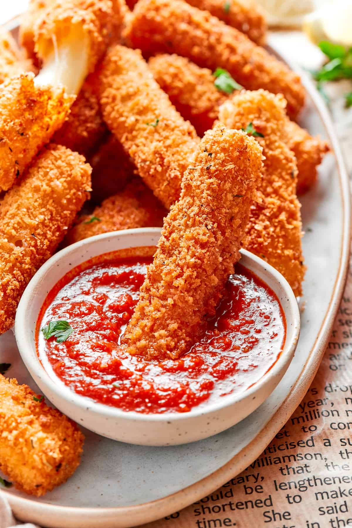 A mozzarella stick being dipped in a bowl of marinara sauce.