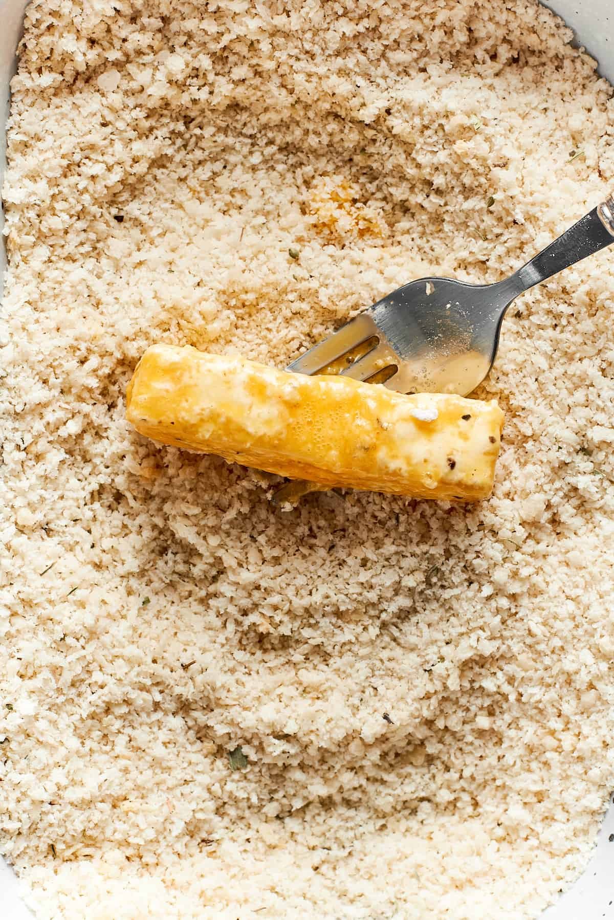 A fork tosses the piece of mozzarella in breadcrumbs.
