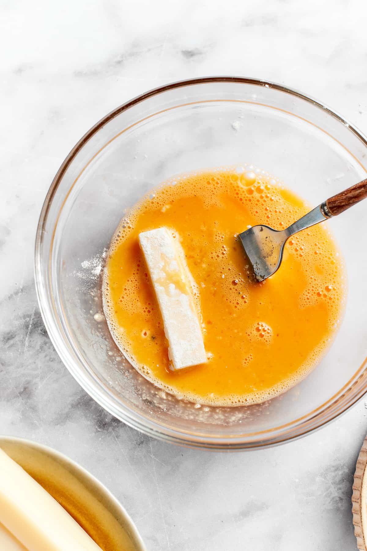 A piece of mozzarella is placed in beaten egg.