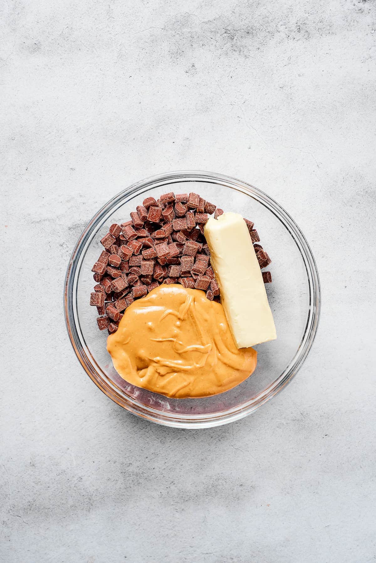Peanut butter, chocolate chunks, and butter in a glass bowl.