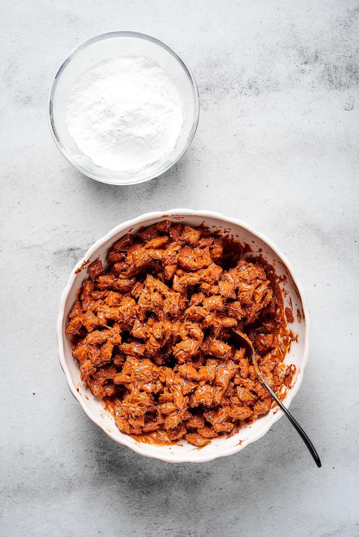 Chex cereal coated in chocolate and peanut butter, with a bowl of powdered sugar nearby.