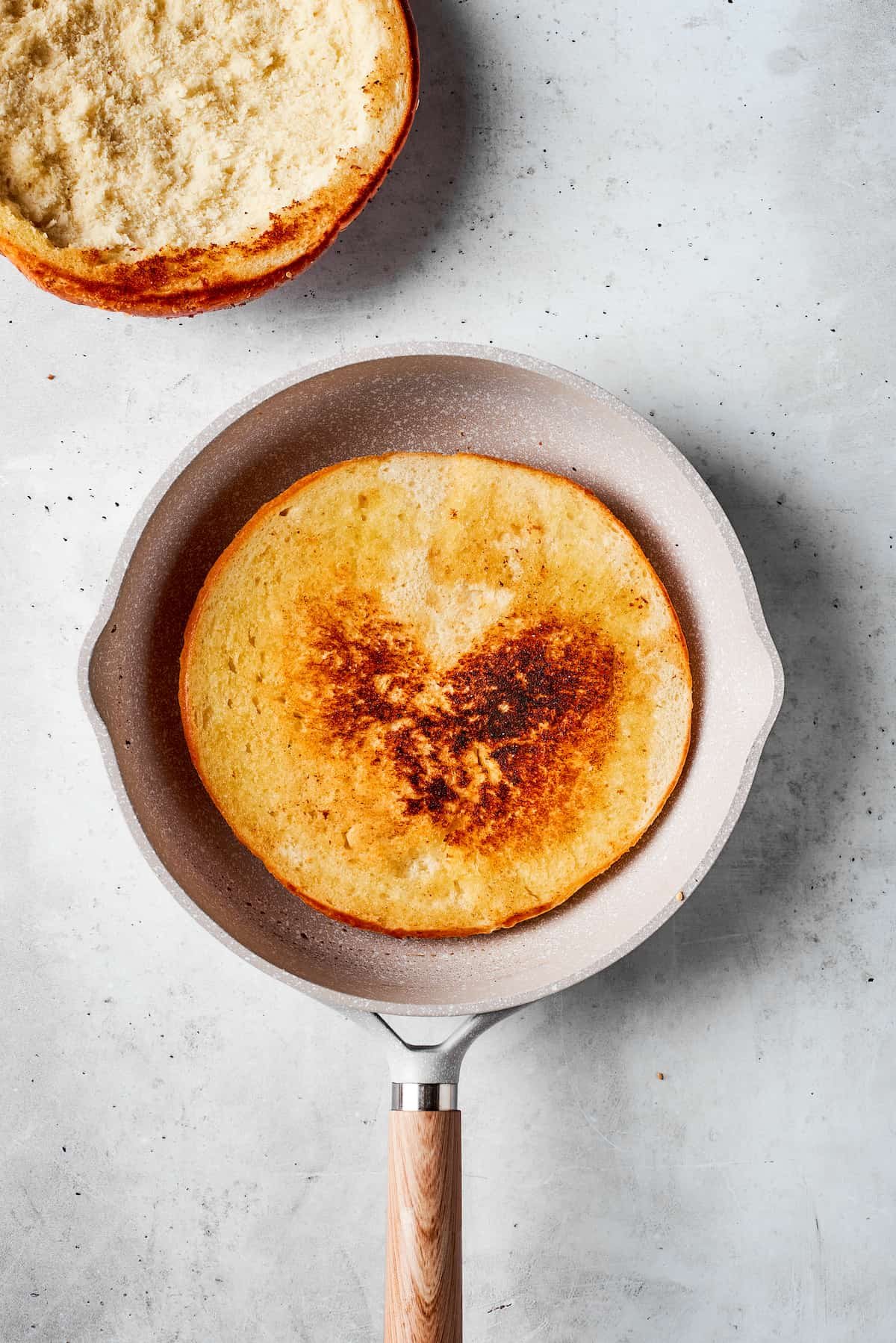 A half of muffaletta bread is toasted in a skillet.