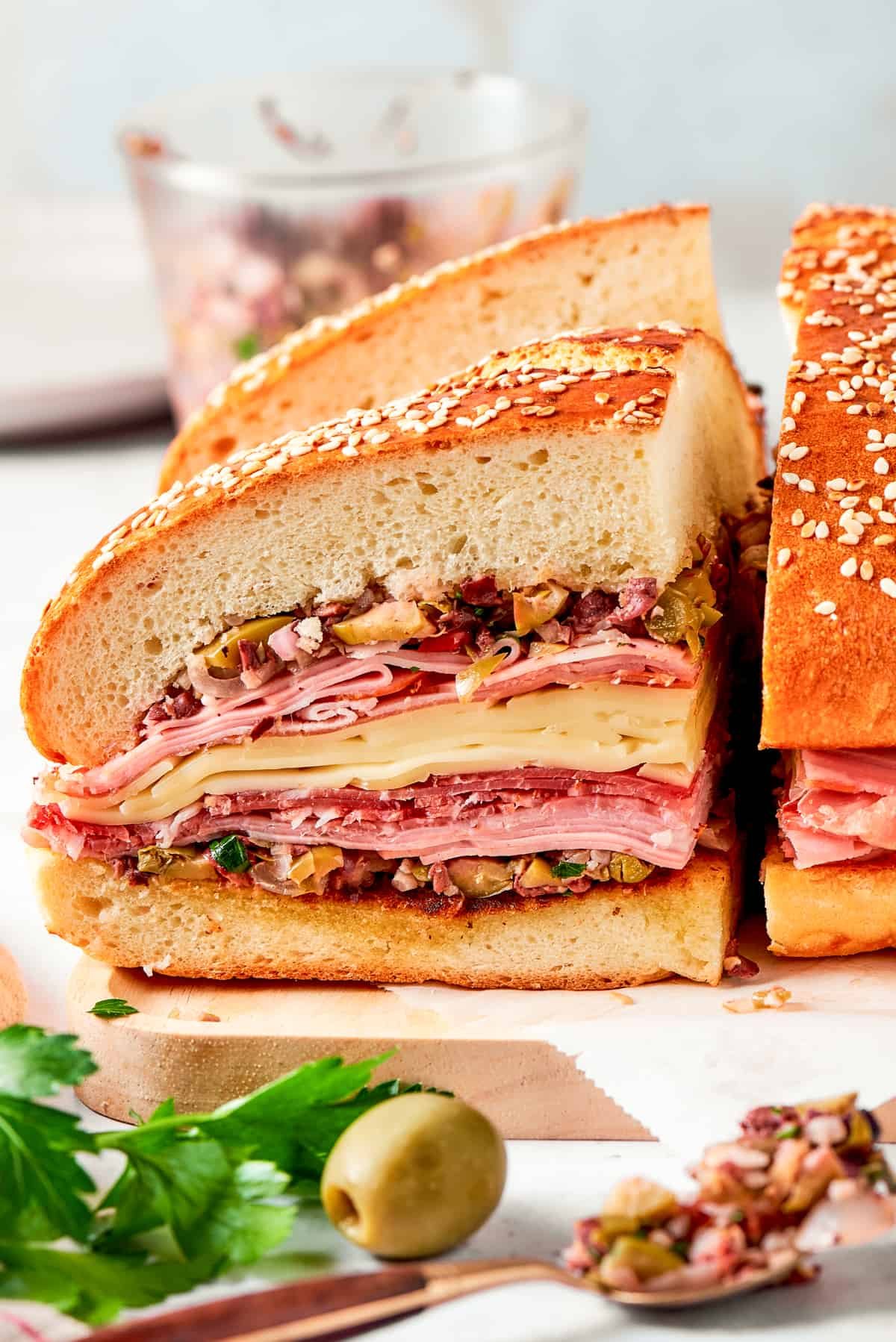 Two pieces of tall muffaletta sandwich on cutting board.