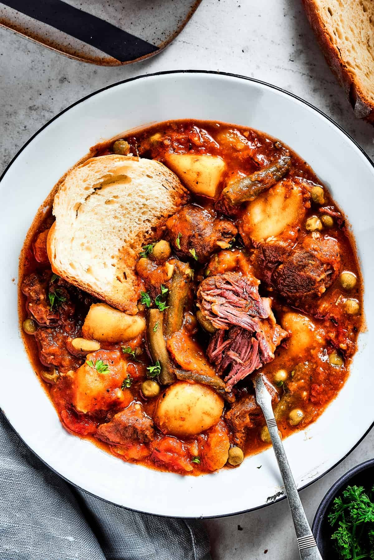 A bowl of stew with a spoon. A chunk of beef has been pulled apart to show the texture.