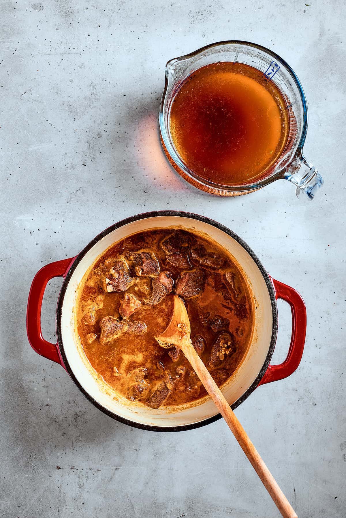 Pouring broth over chunks of beef in a pot.