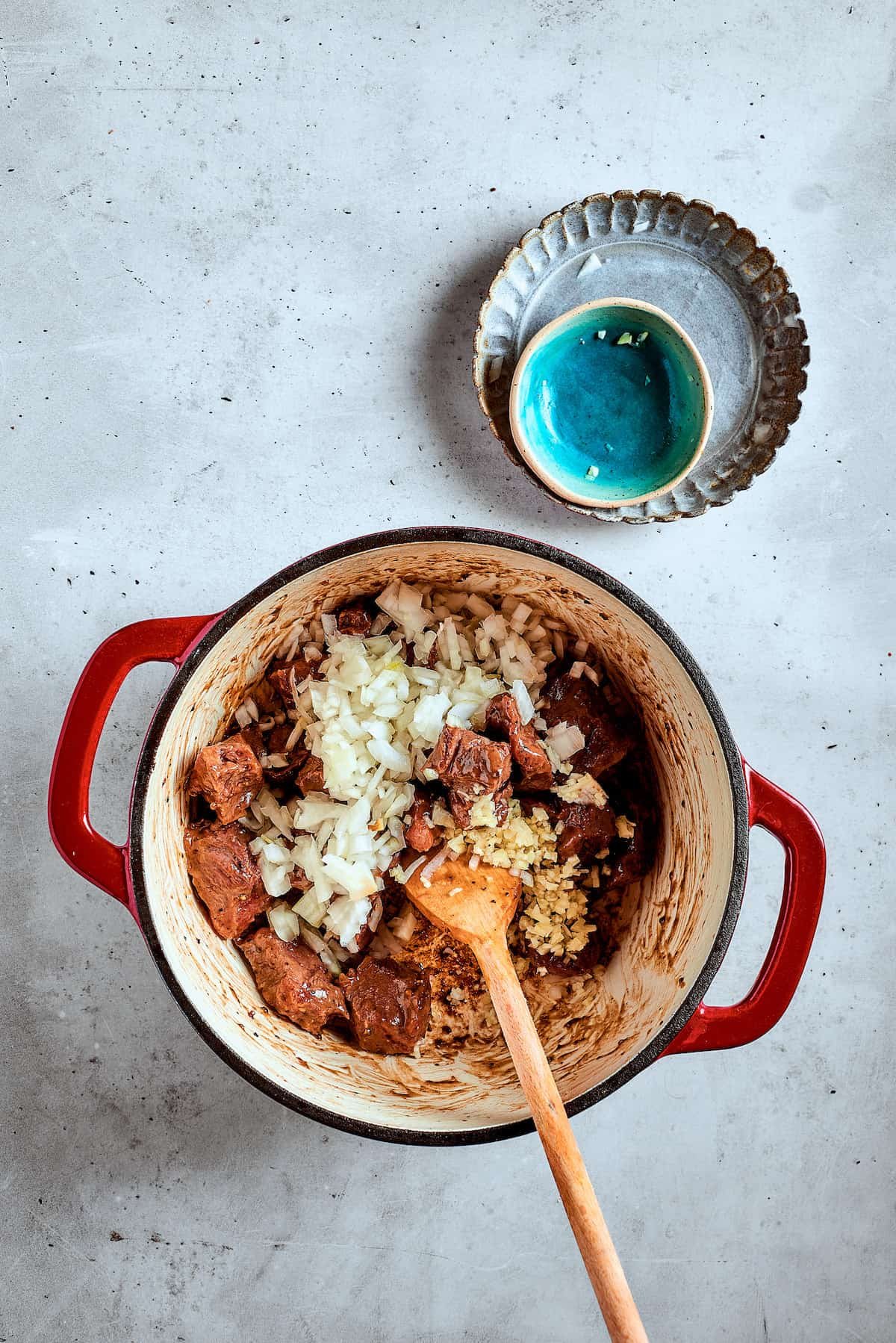 Adding onion and garlic to a pot of browned beef.