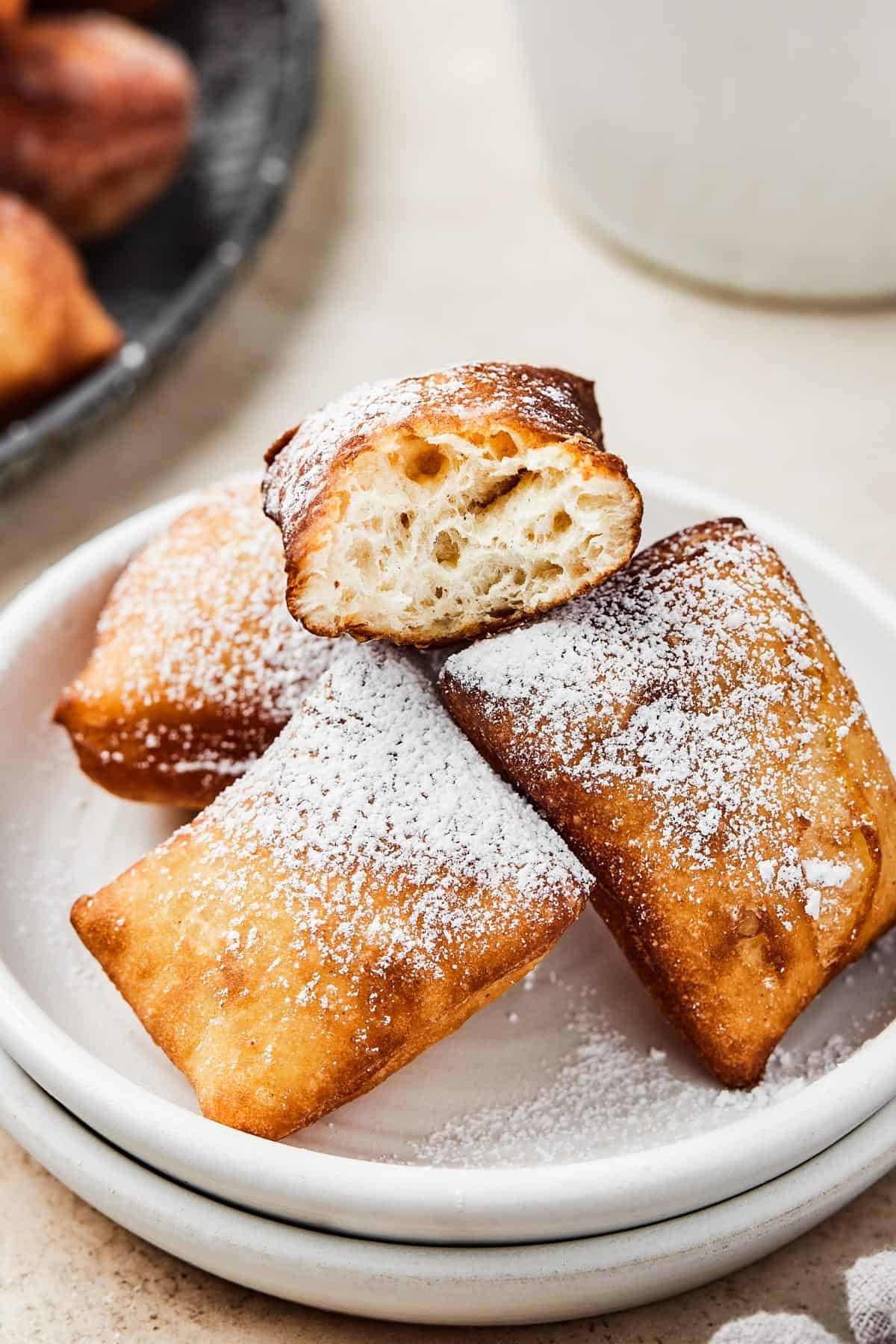 Homemade square donuts on a plate. One has been broken in half to show the fluffy texture of the interior.