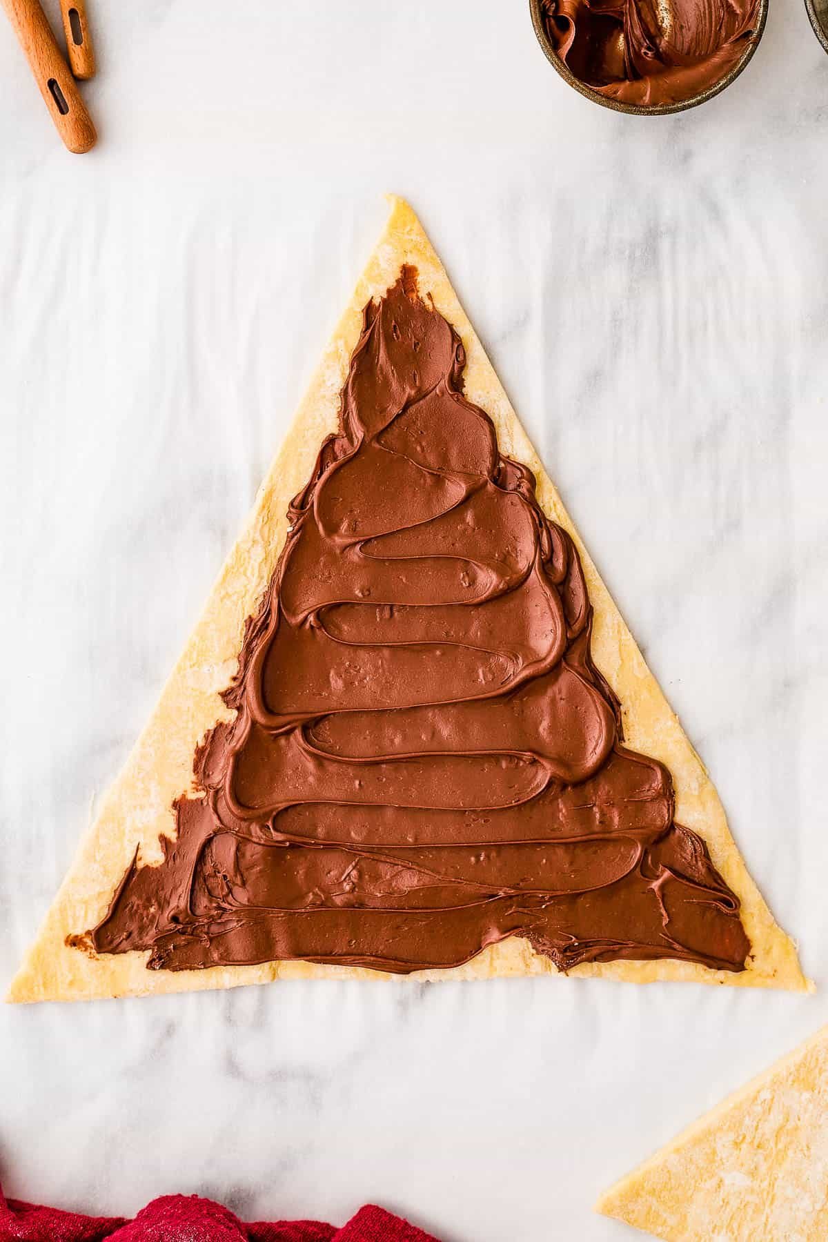 A triangle of puff pastry dough, spread with hazelnut spread.