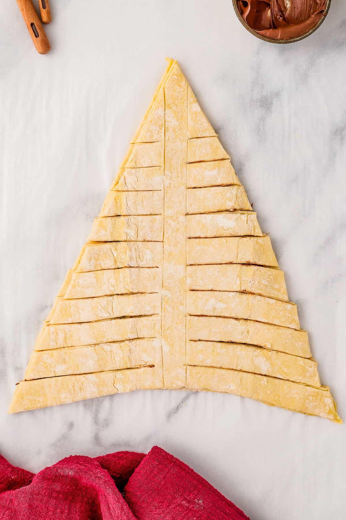 The cut-out triangle of puff pastry, filled with Nutella, with horizontal cuts along either side.