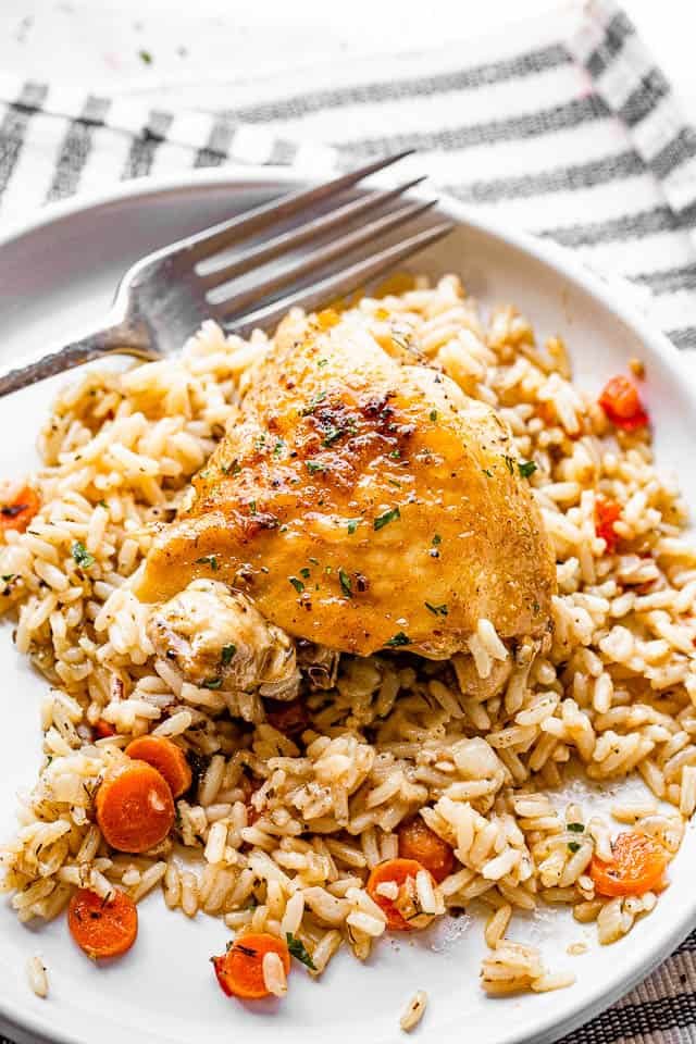 skin-on chicken thighs served over rice in a white plate with fork on the side