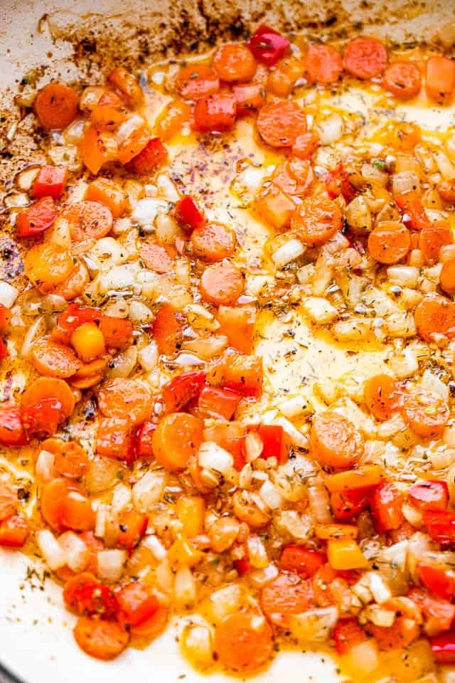 frying carrots and onions in a white skillet