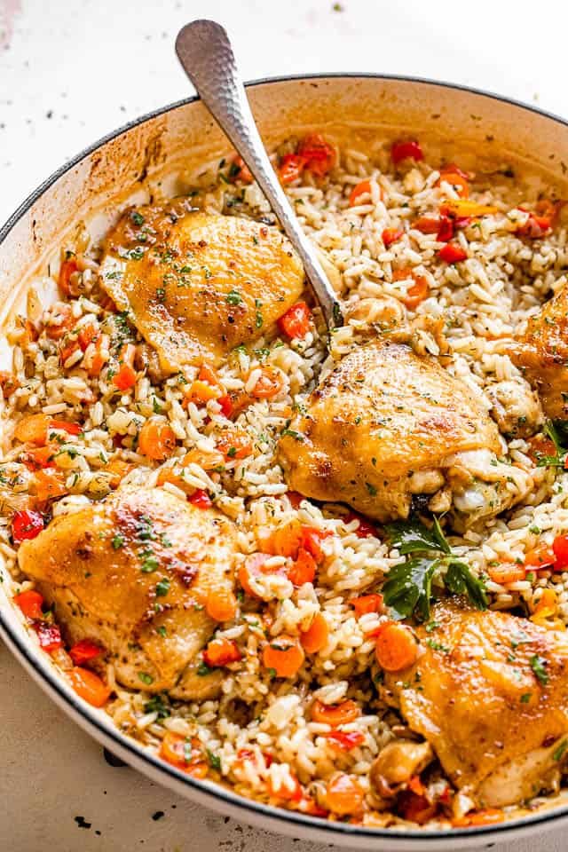 scooping out chicken thighs set on a bed of rice inside a white skillet