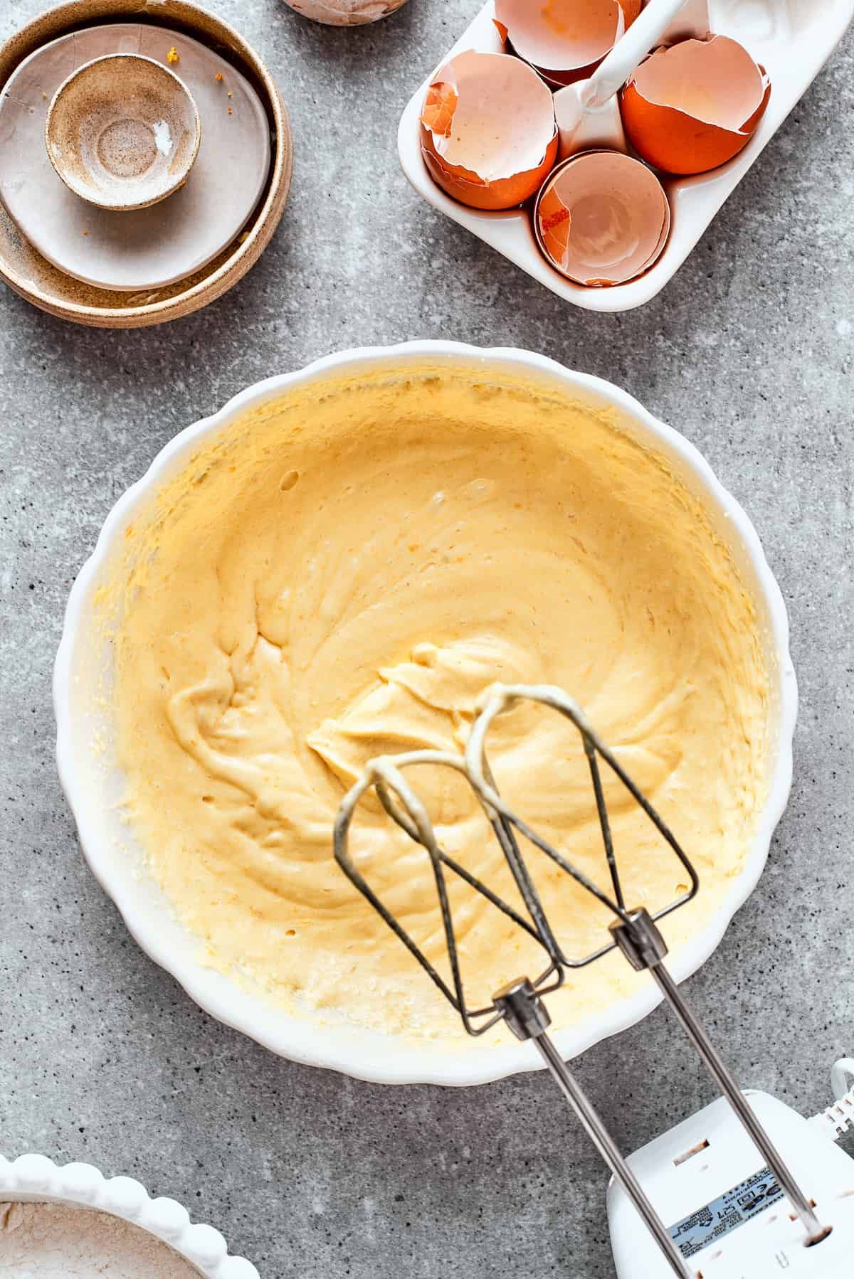 A hand mixer beats the batter for orange cake in a white bowl.