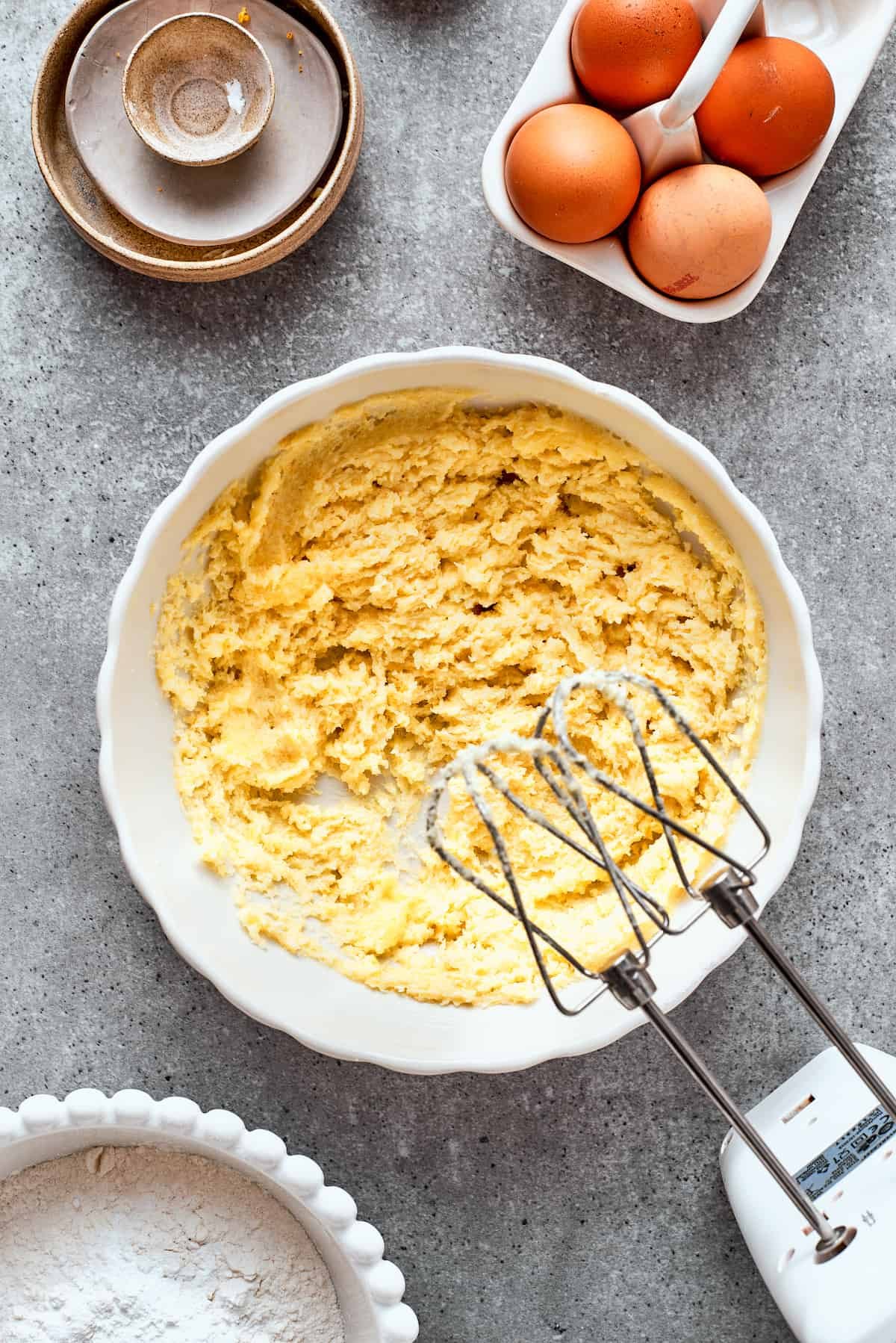 A hand mixer creams butter and sugar in a white bowl.