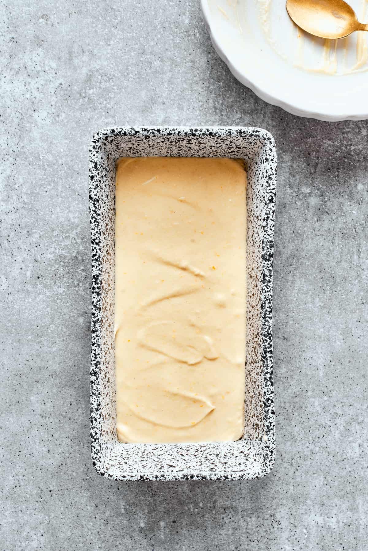 Orange cake batter is smoothed into a metal loaf pan.