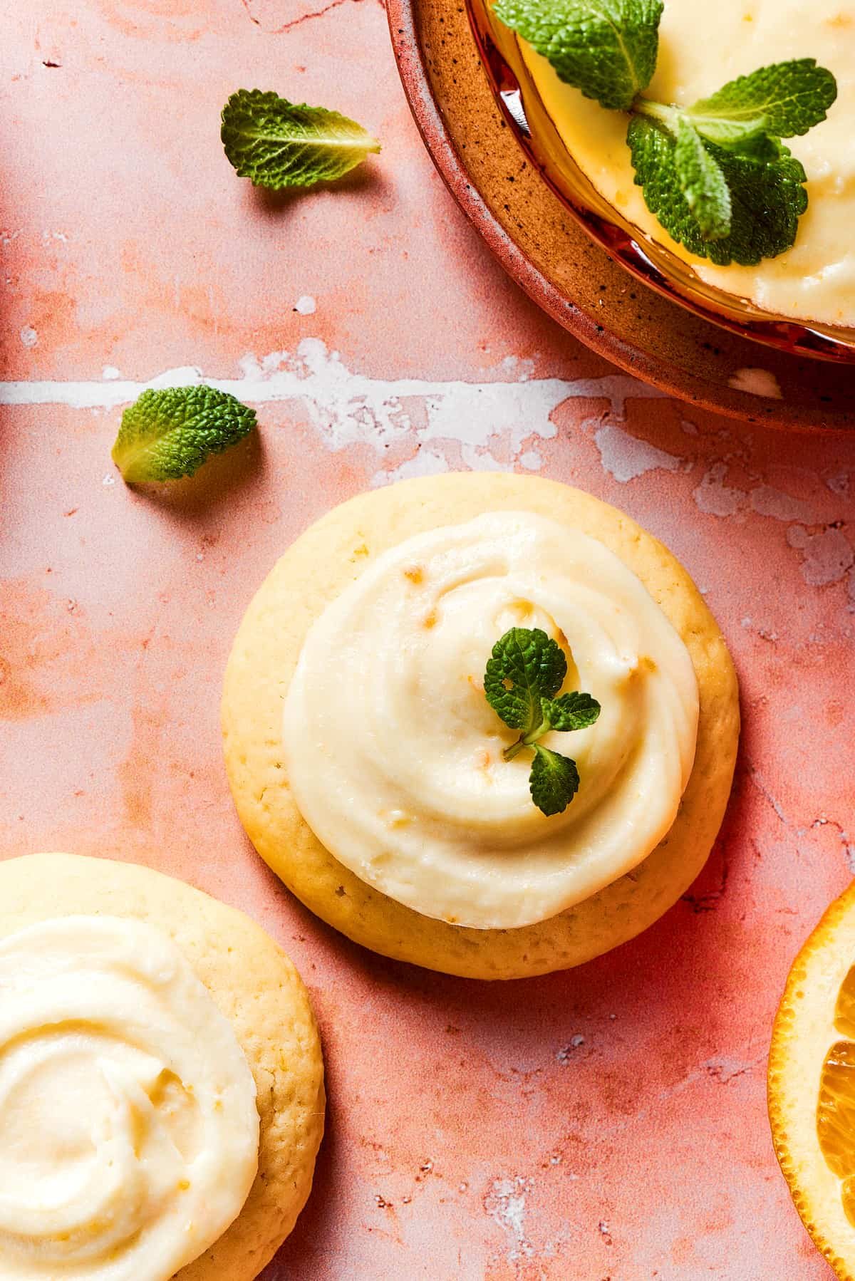 Three orange cookies garnished with fresh herbs, on a tile table.