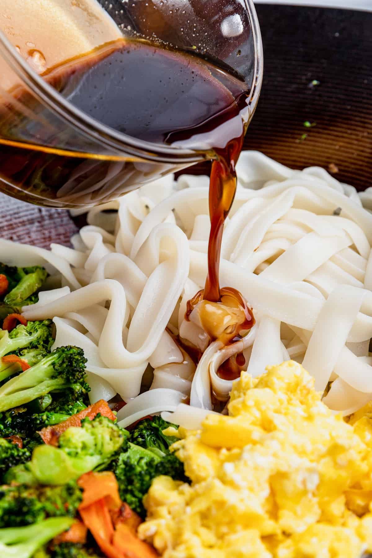 Pad See Ew Sauce Being Added to the Noodles, Eggs and Veggies in the Bowl