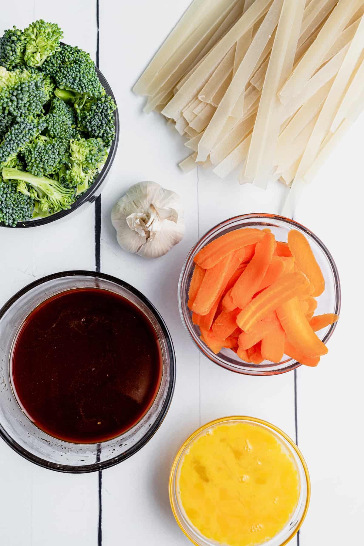 Broccoli, Flat Rice Noodles, Carrot Slices and the Rest of the Ingredients on Top of a White Picnic Table