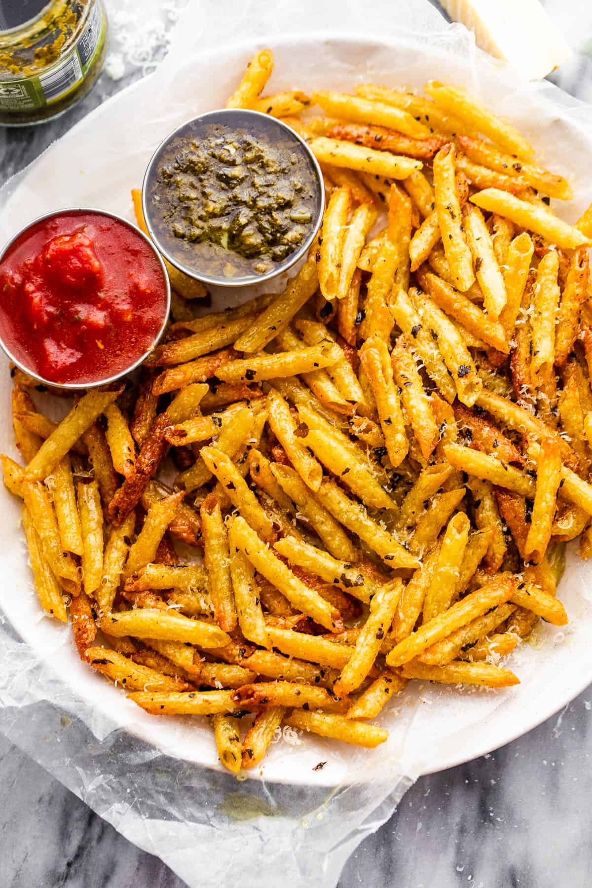 plate with baked pasta chips served with a side of basil pesto and marinara sauce