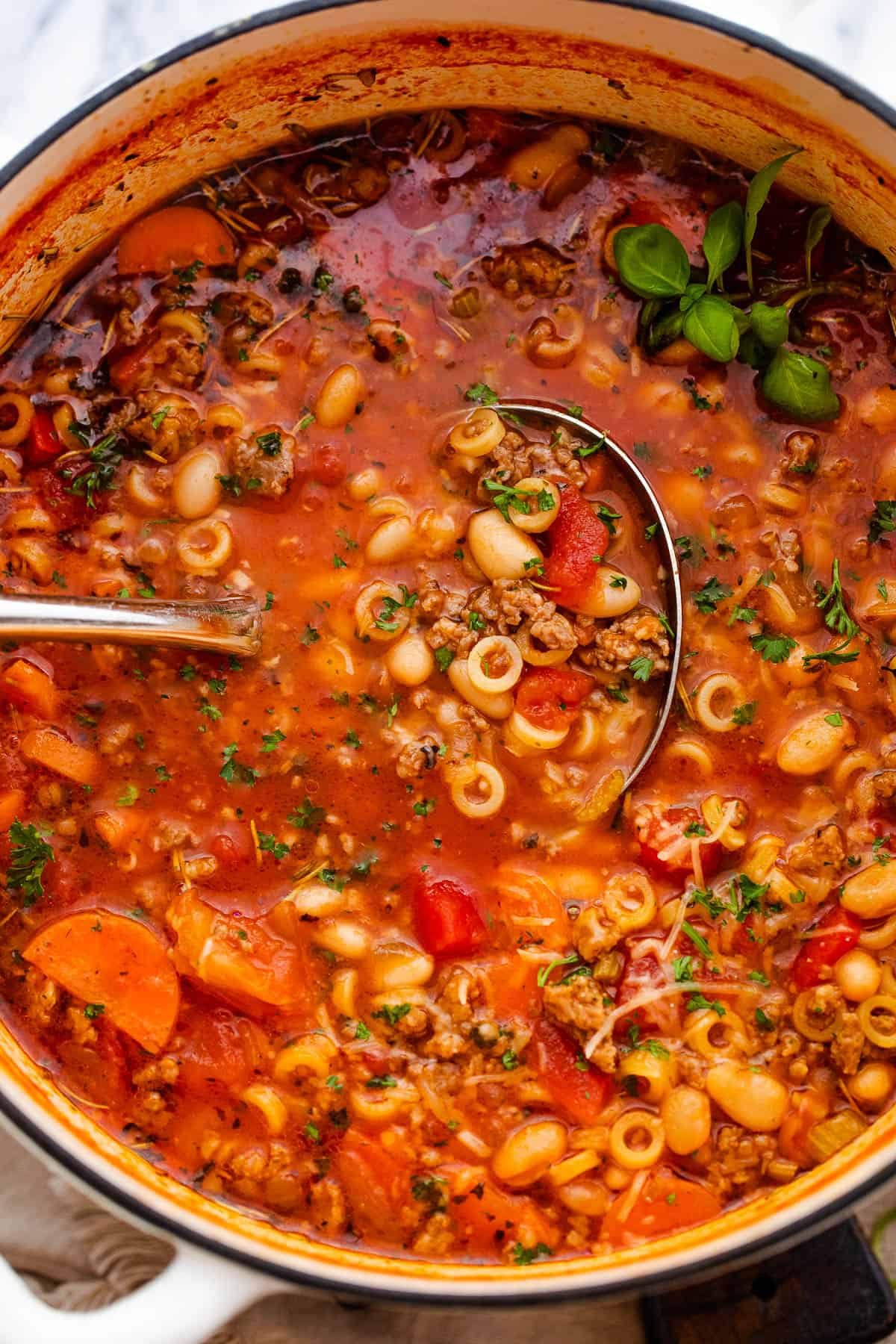 pasta fagioli soup in a white dutch oven with ladle inside the soup