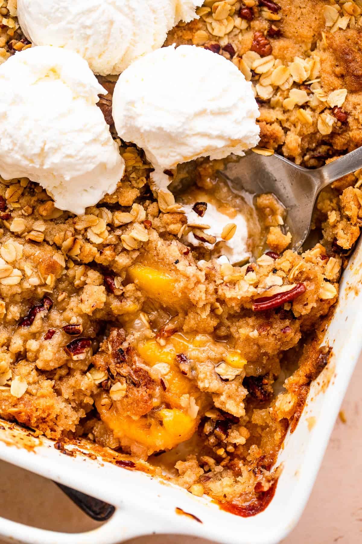 peach crisp in a white baking dish topped with three scoops of vanilla ice cream