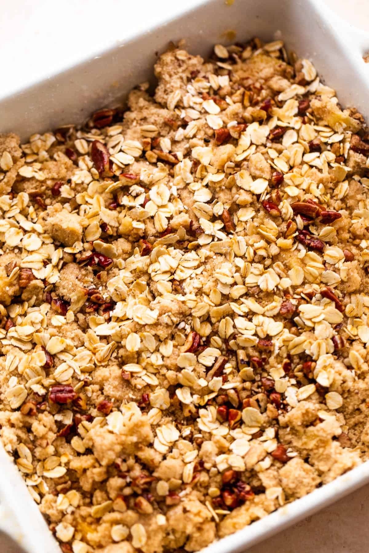 squared baking dish with peach slices covered in oats, flour, and pecans
