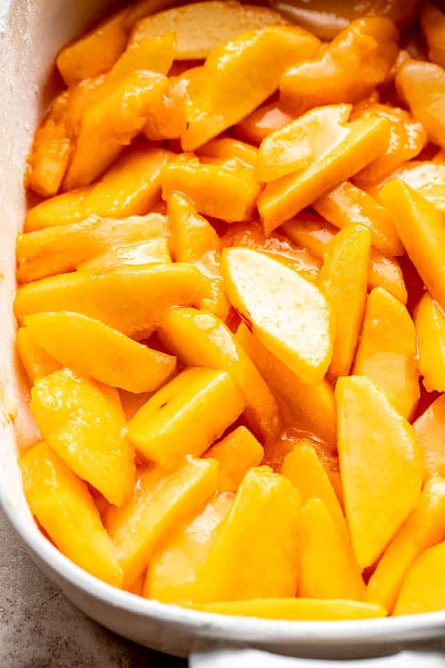 Sliced peaches in a baking dish prepped for a cake.