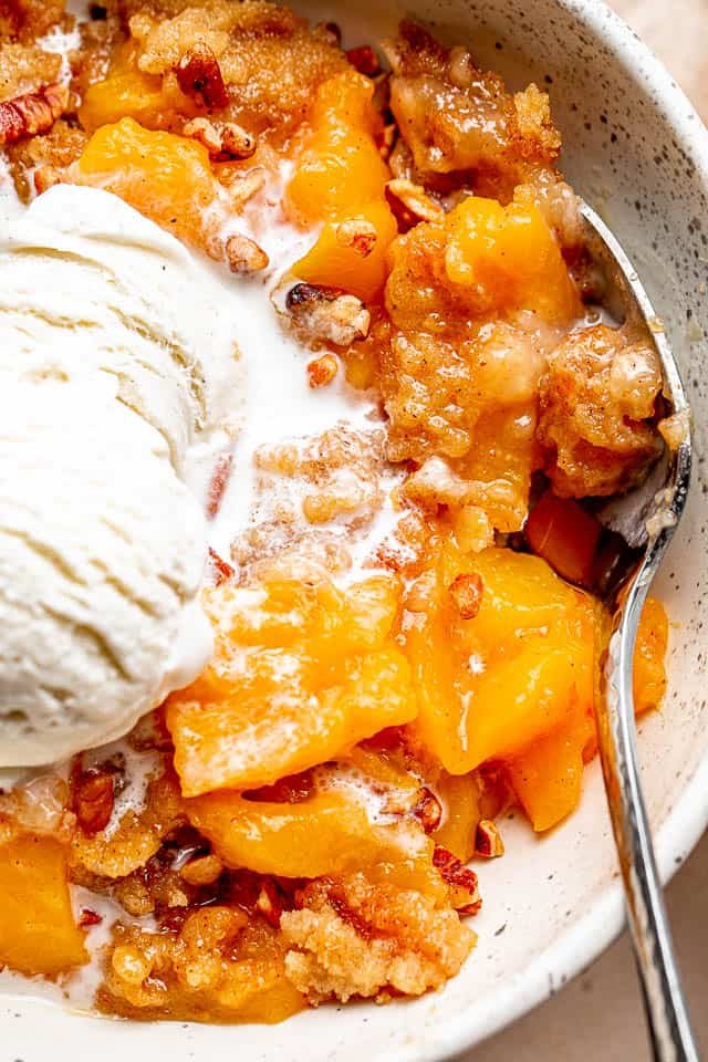 A spoon resting in a white bowl with a Peach Cake and a scoop of ice cream.