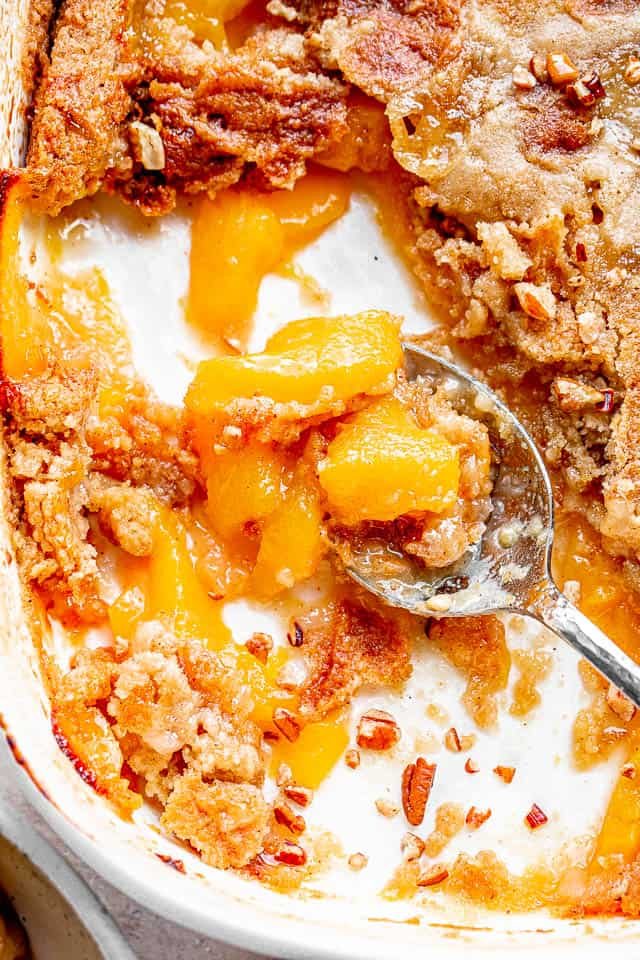 top shot of silver spoon scooping out a peach cake from white baking dish