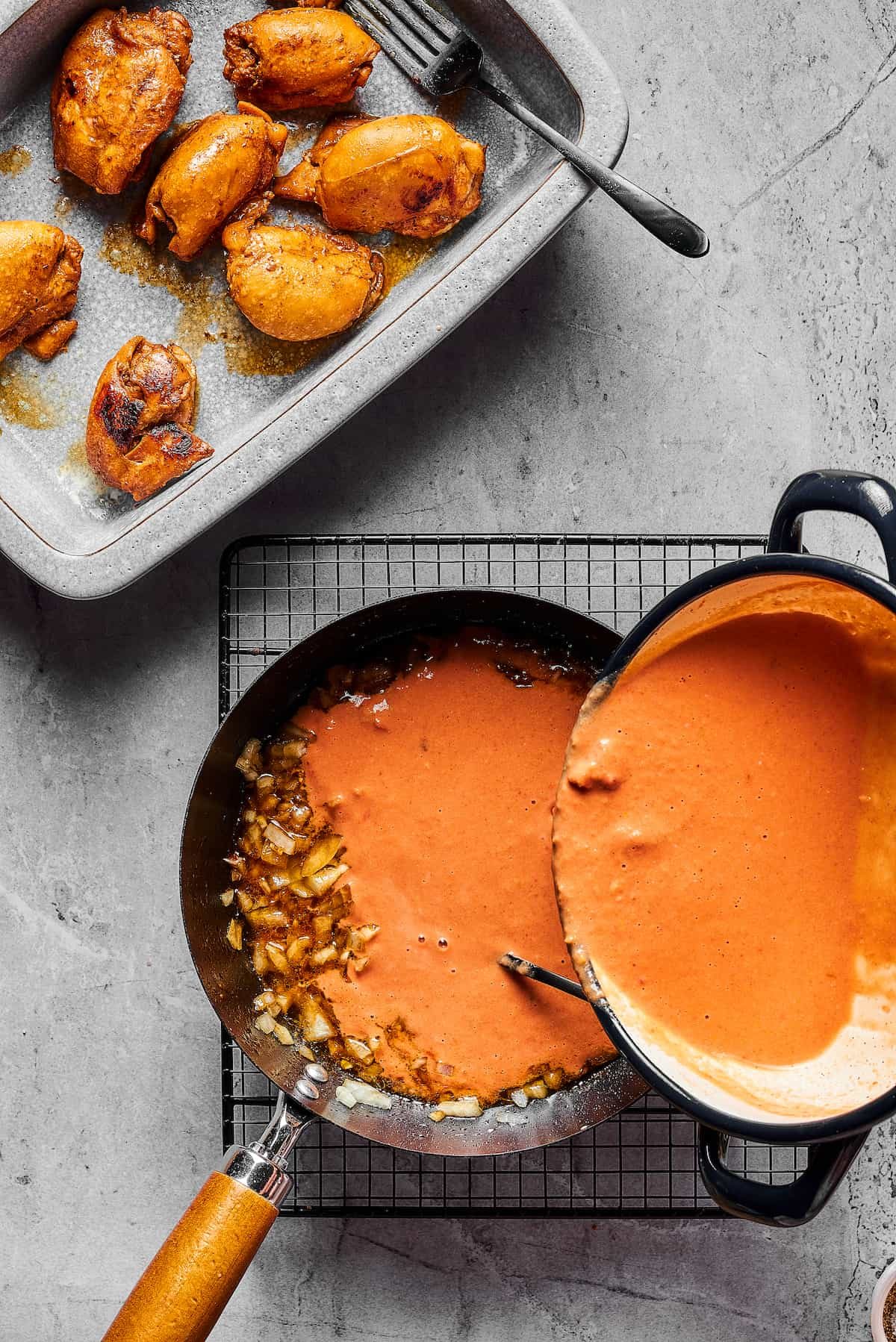 Chopped onions in a skillet. Peanut sauce is being poured over the onions, and a platter of cooked chicken sits nearby.