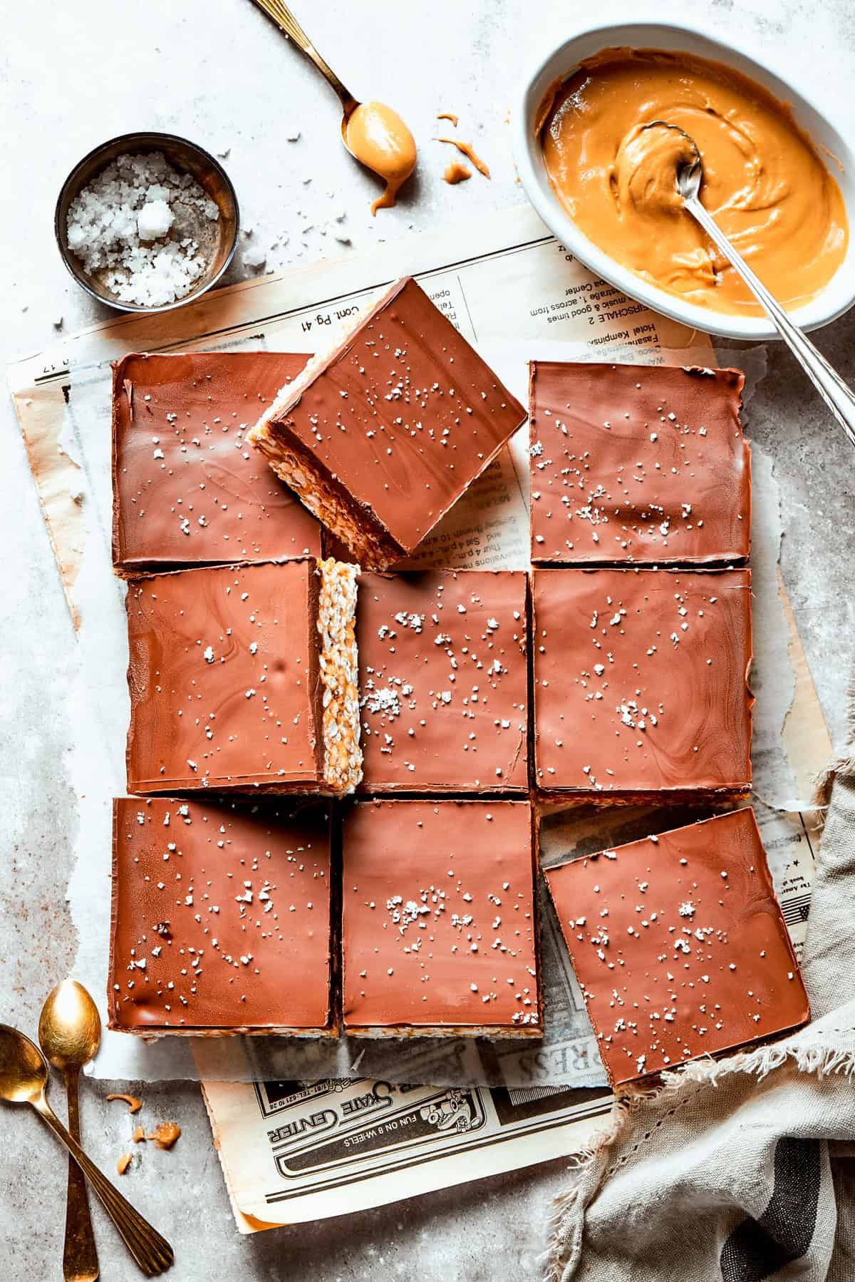 Rice crispy treats cut into squares with a bowl of peanut butter and a bowl of salt nearby.