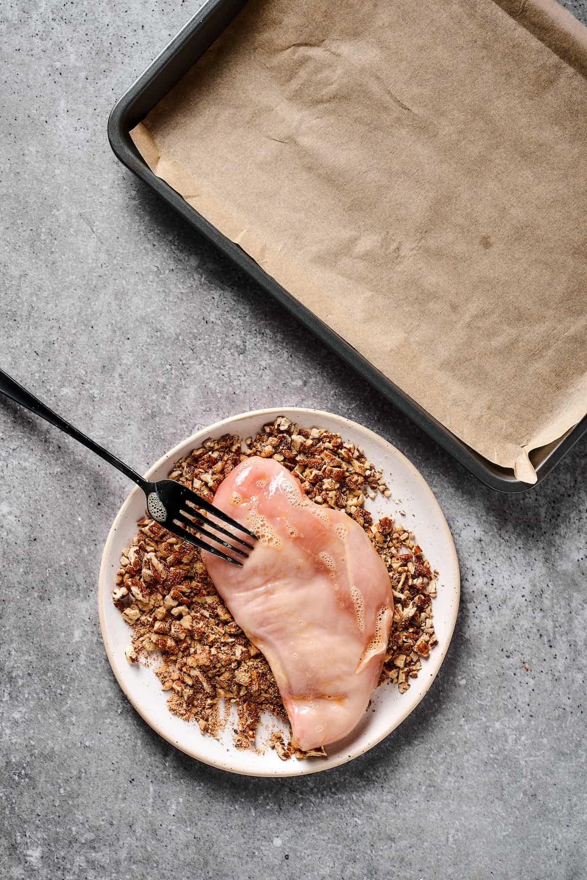 Raw chicken being coated in a ground pecan mixture.