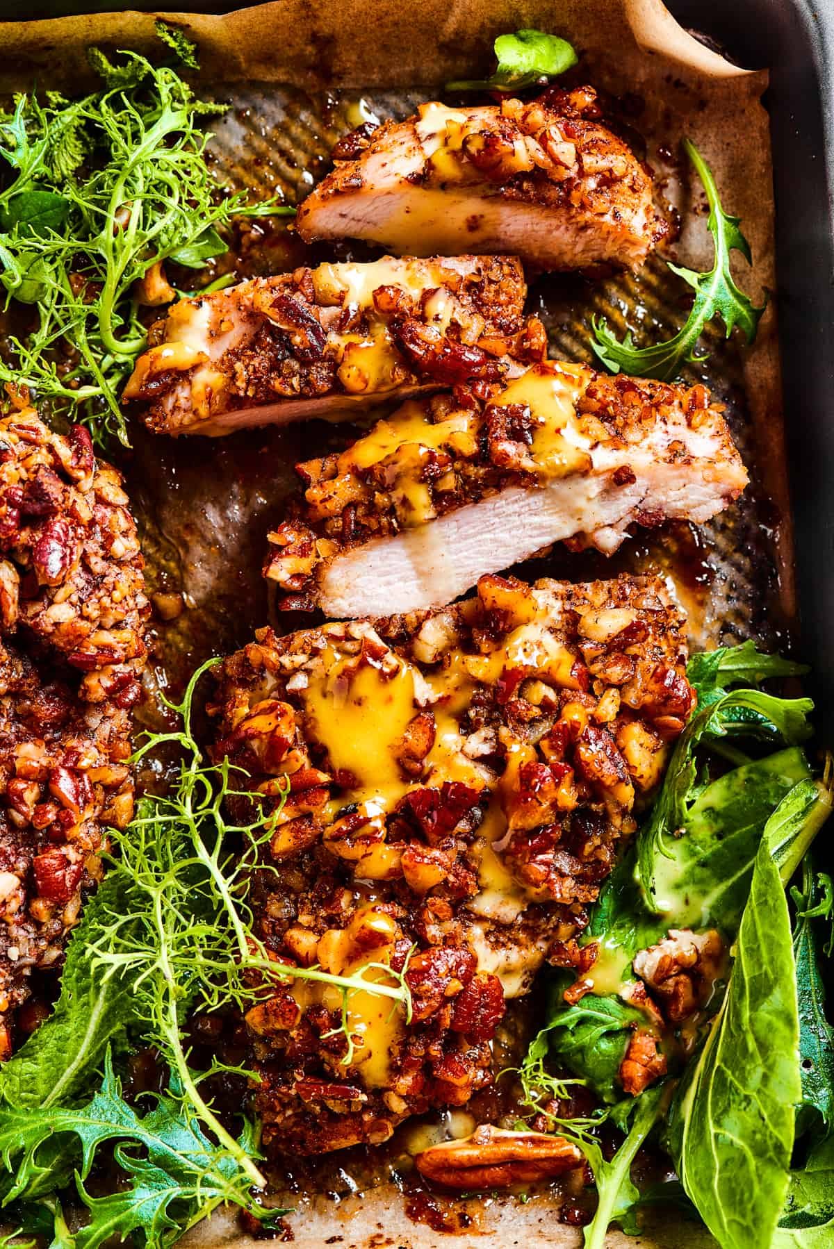 Sliced pecan chicken on a serving dish, with greens placed around the chicken.