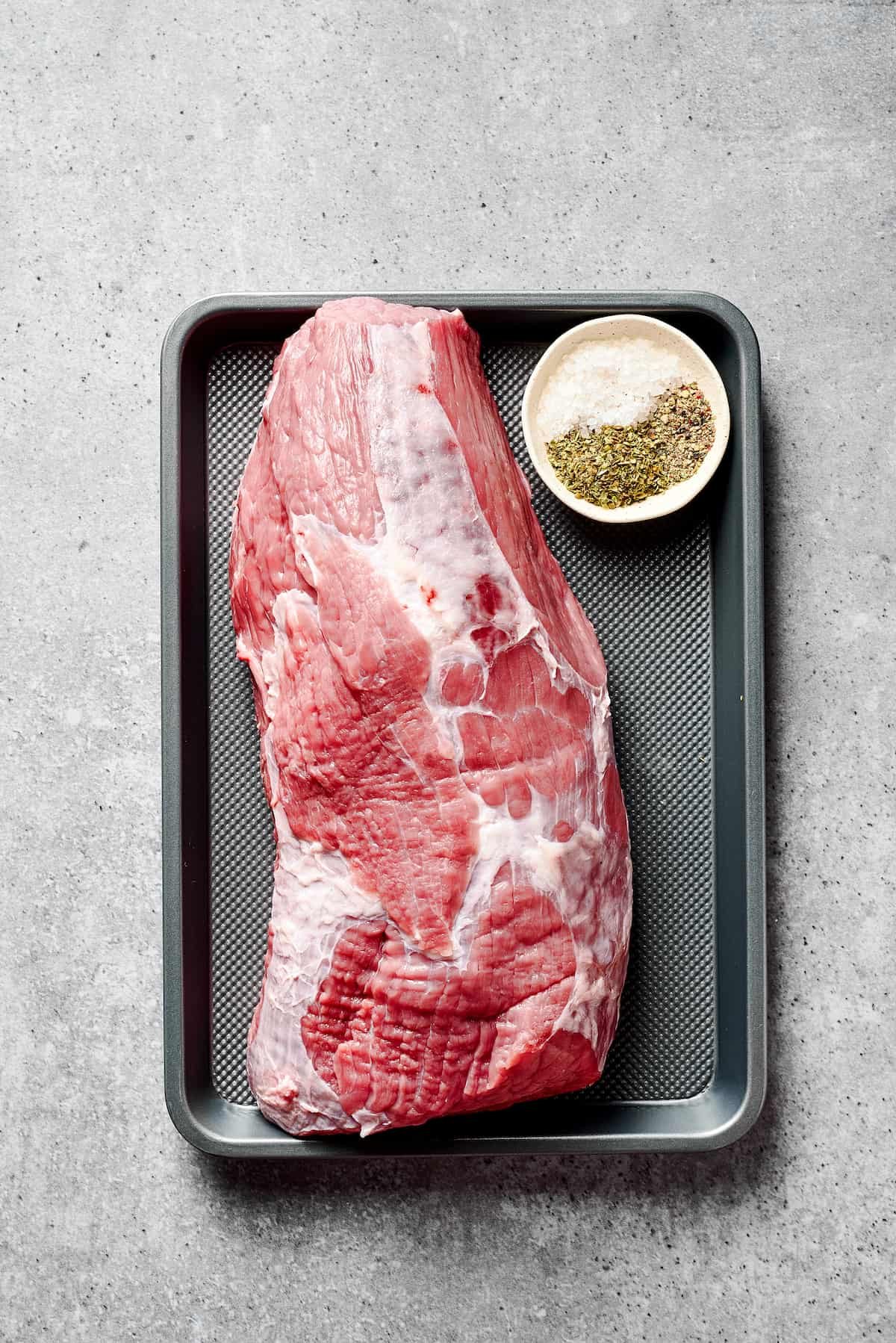 A large rump roast on a tray with a small dish of seasonings.