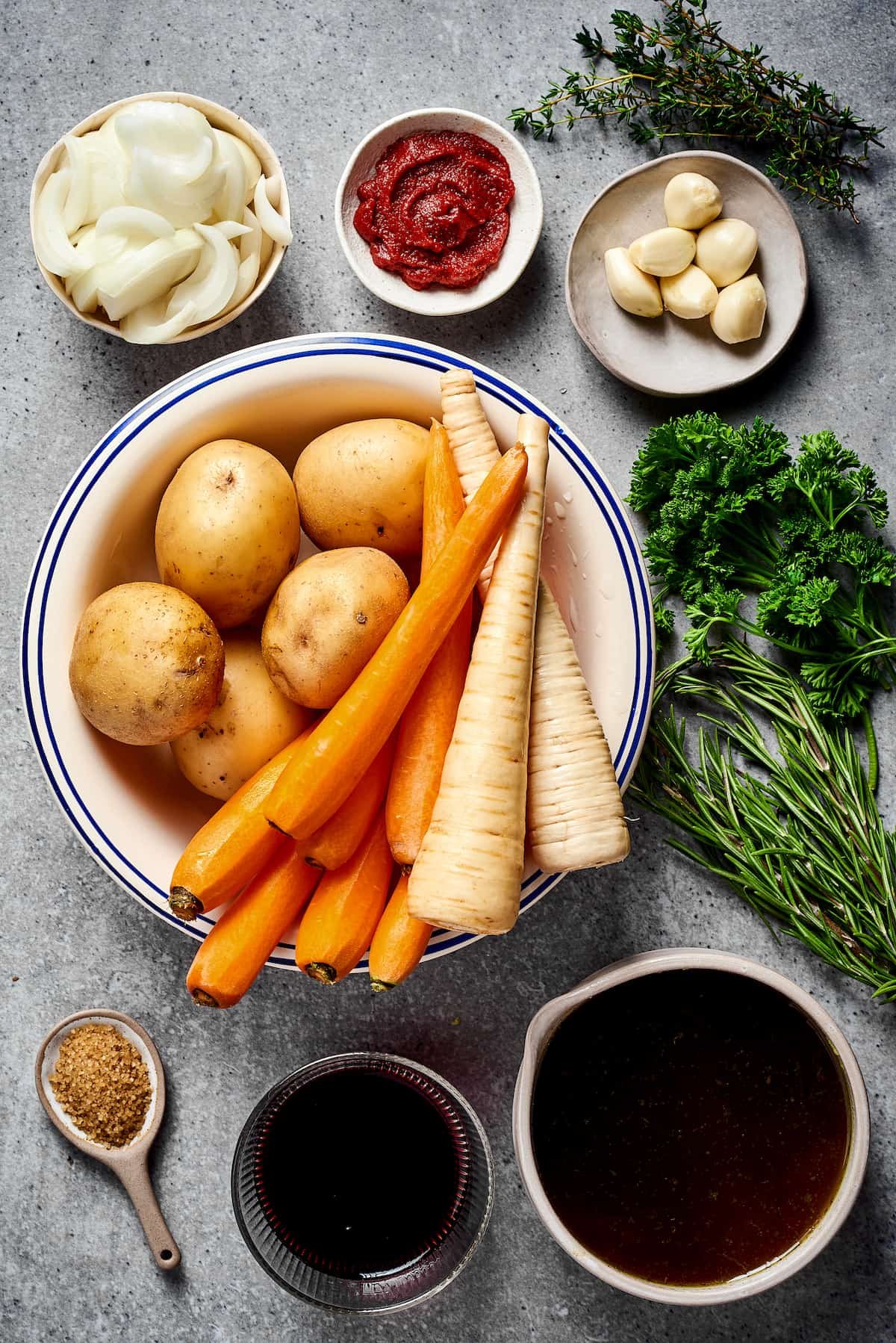 From top left: onion, tomato paste, garlic, potatoes, carrots, parsnips, fresh herbs, seasonings, red wine, beef broth.