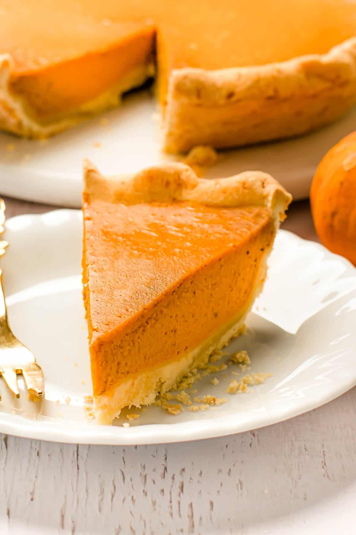 A pumpkin pie slice on a white plate with a fork.