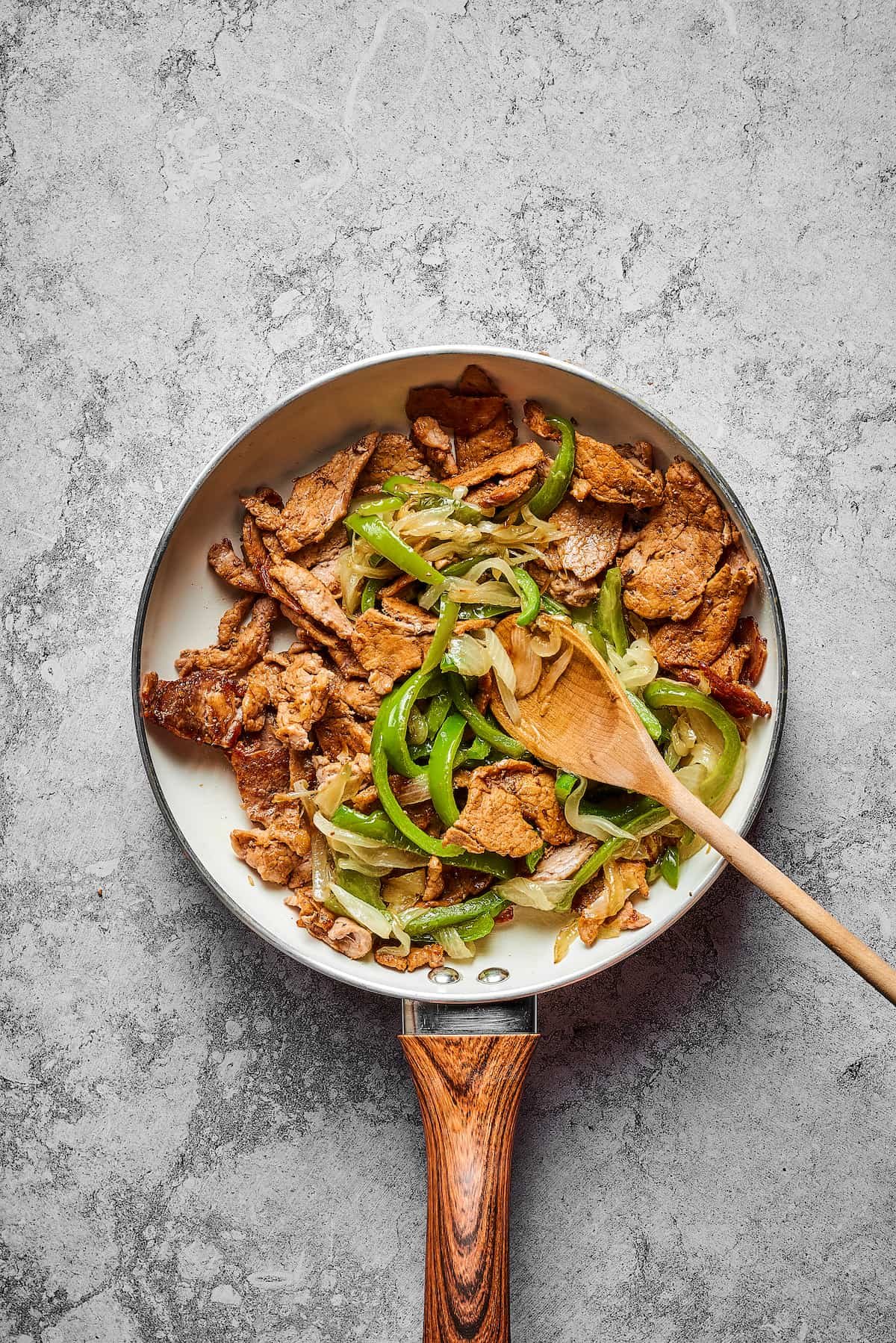 Sliced steak, onion, and bell pepper cooking in a skillet.