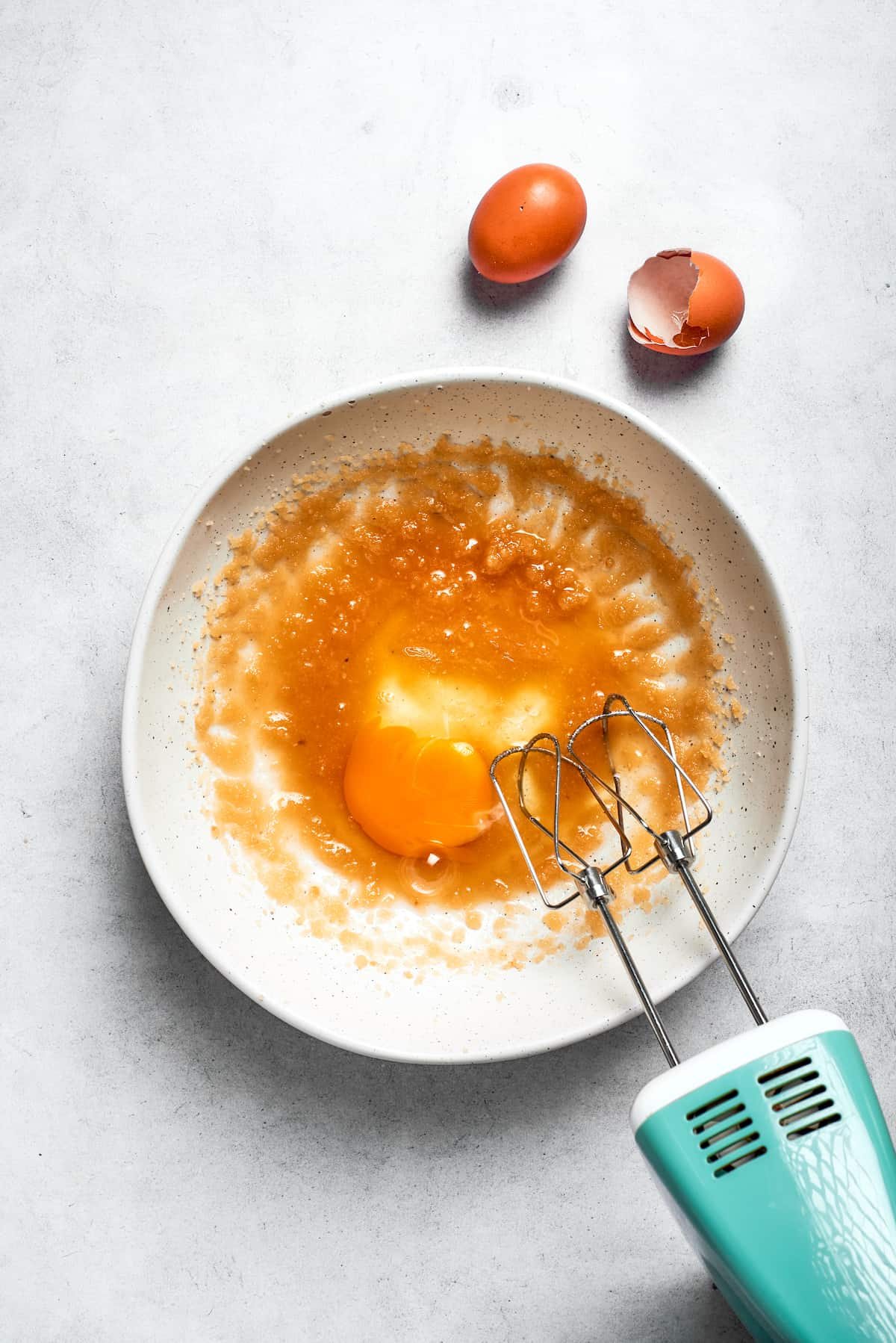 A hand mixer beats in the eggs.