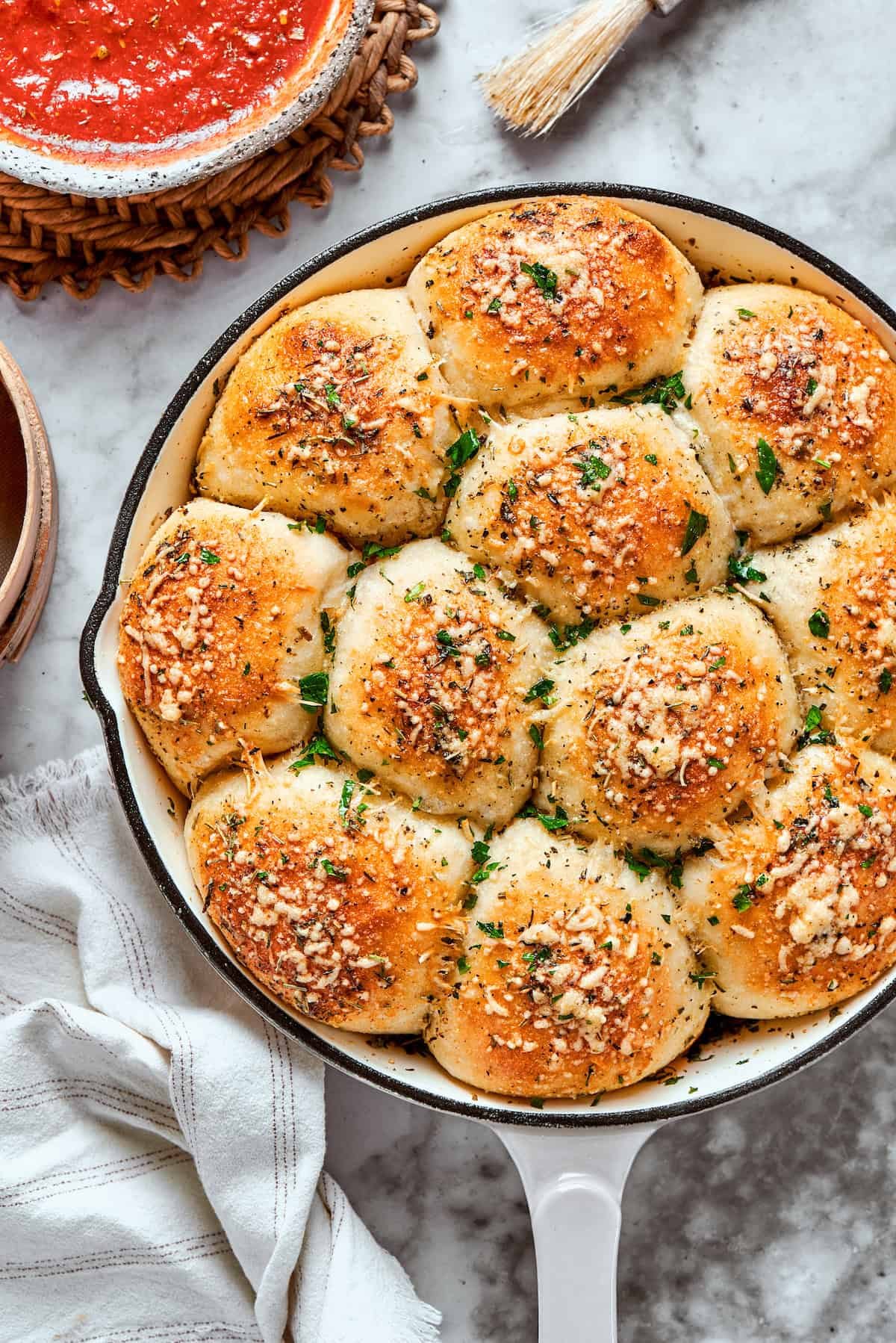 A skillet of baked pizza bites next to a bowl of sauce.