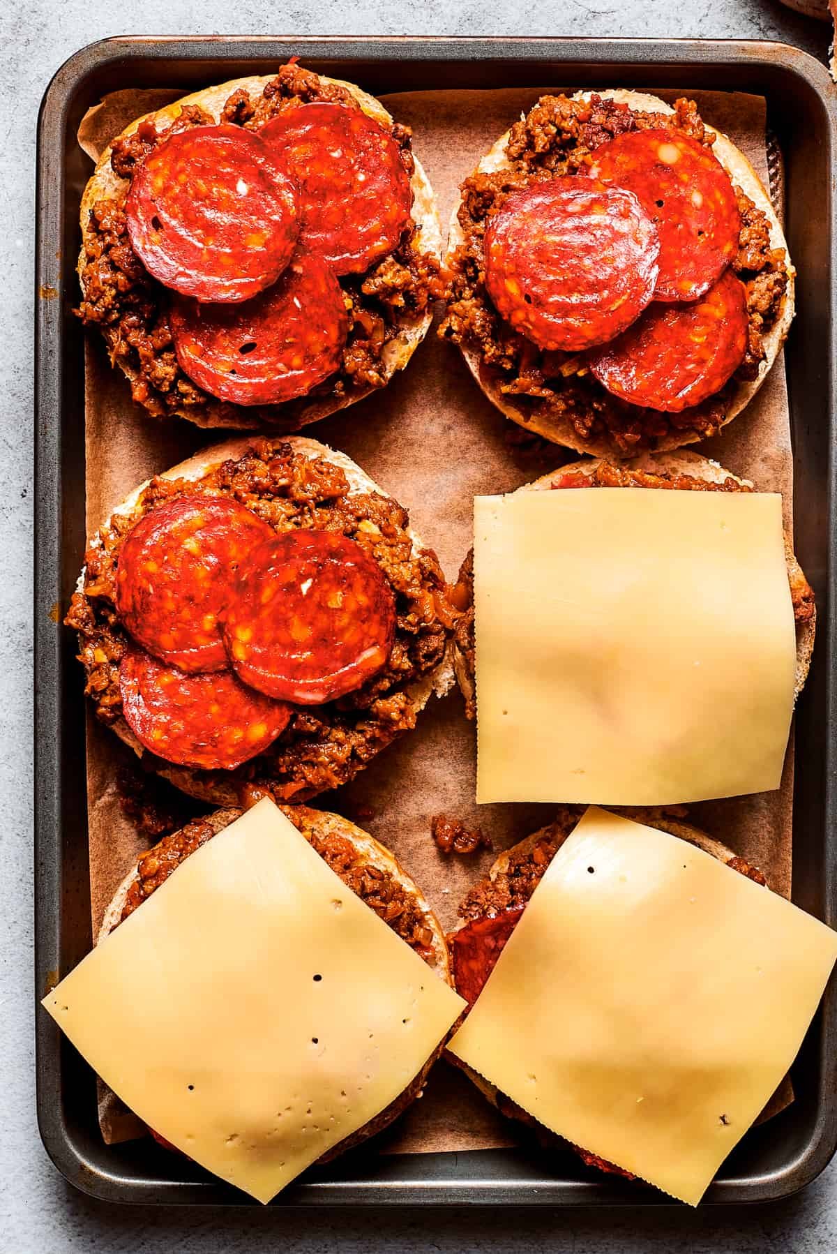 Cheese slices are placed on top of pizza burgers on a tray.