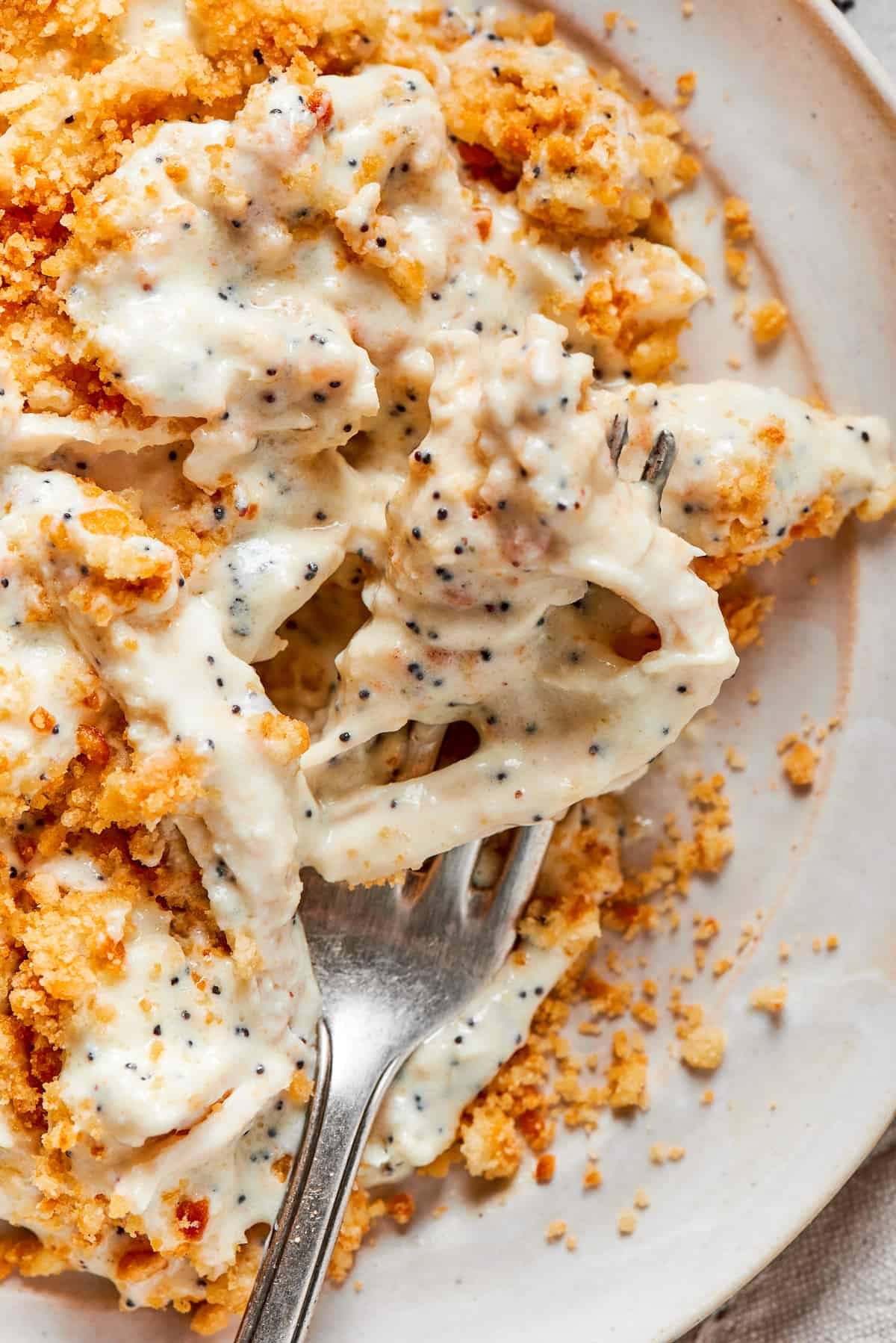 A fork shows a chunk of poppy seed chicken above a plate of the dish.
