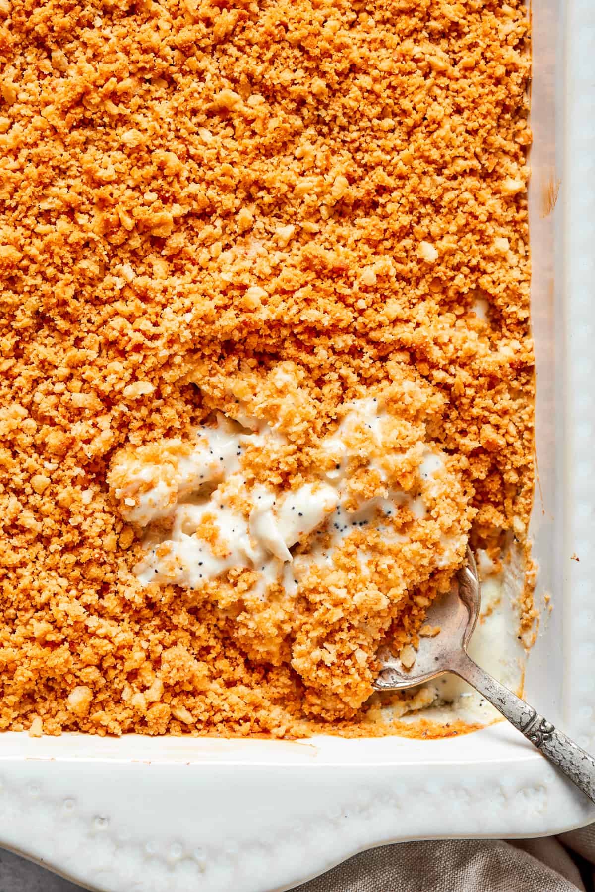 A serving spoon digs into a dish of poppy seed chicken topped with crushed Ritz crackers.