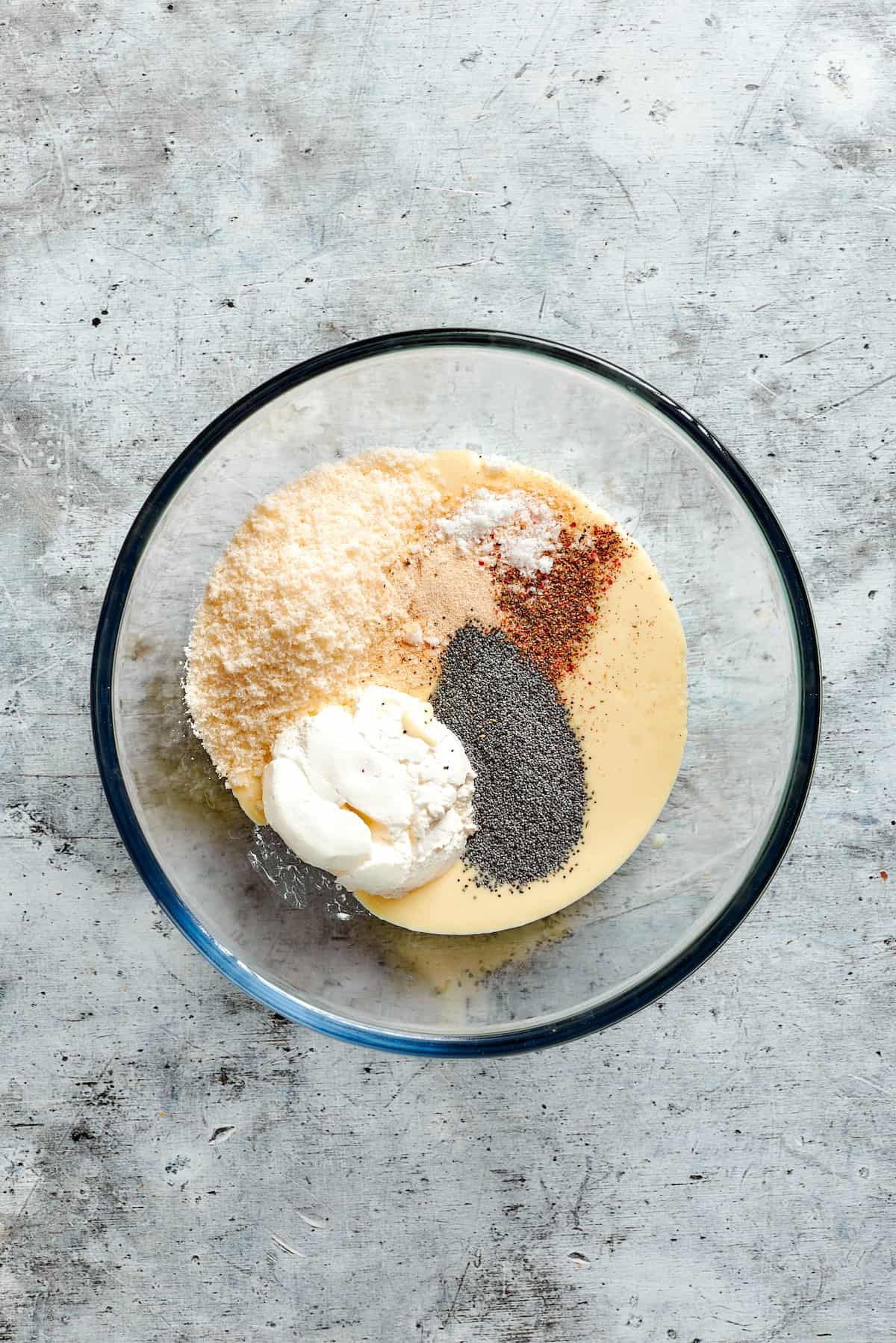 Sour cream, parmesan, cream of chicken soup, spices, and poppy seeds are combined in a bowl.