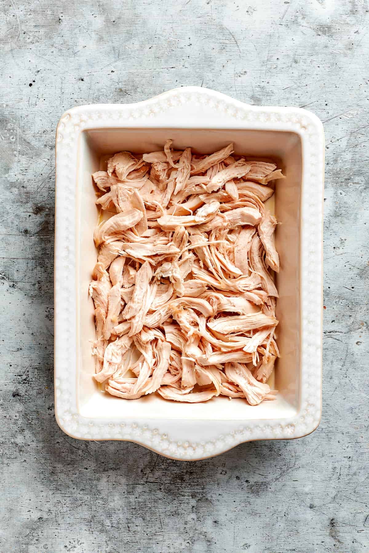 Shredded chicken is arranged in a baking dish.