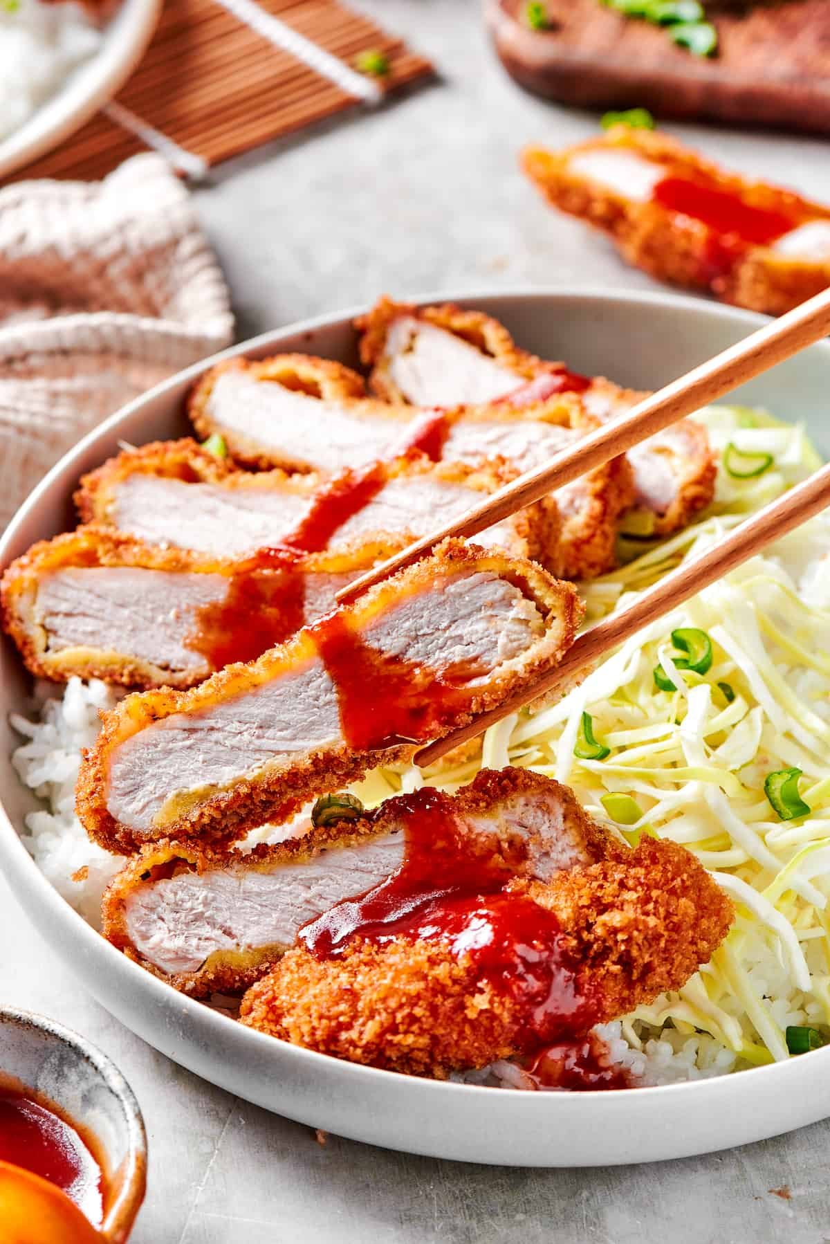 Chopsticks picking up a piece of pork katsu.
