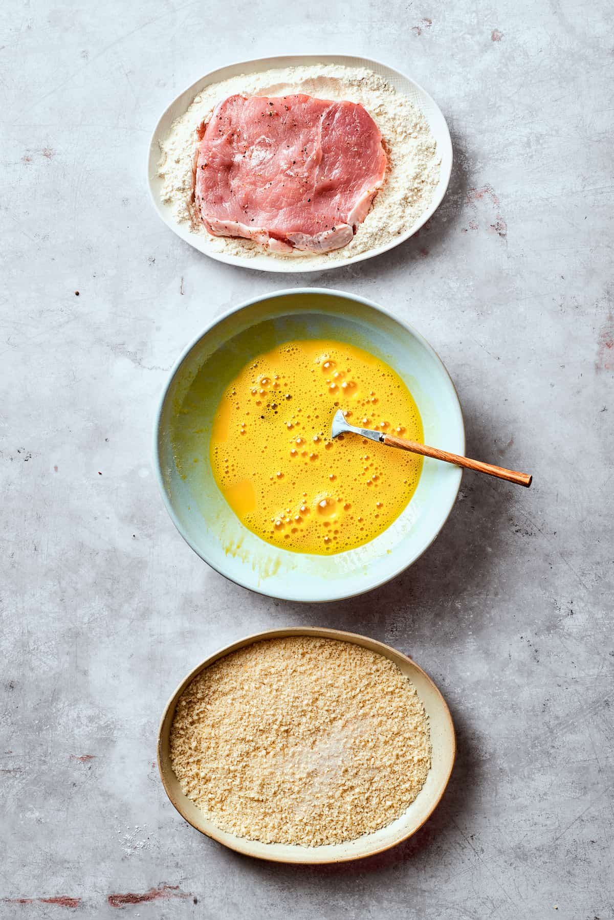 Breading station set up with a bowl of beaten eggs, a bowl of flour, and a bowl of panko.