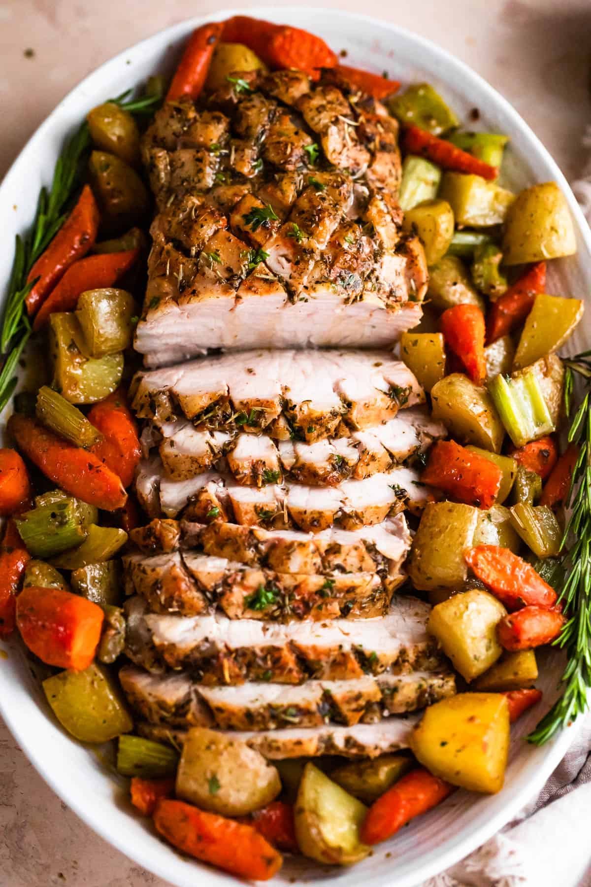 overhead shot of oval plate with cooked and sliced pork loin roast and roasted vegetables arranged around the roast
